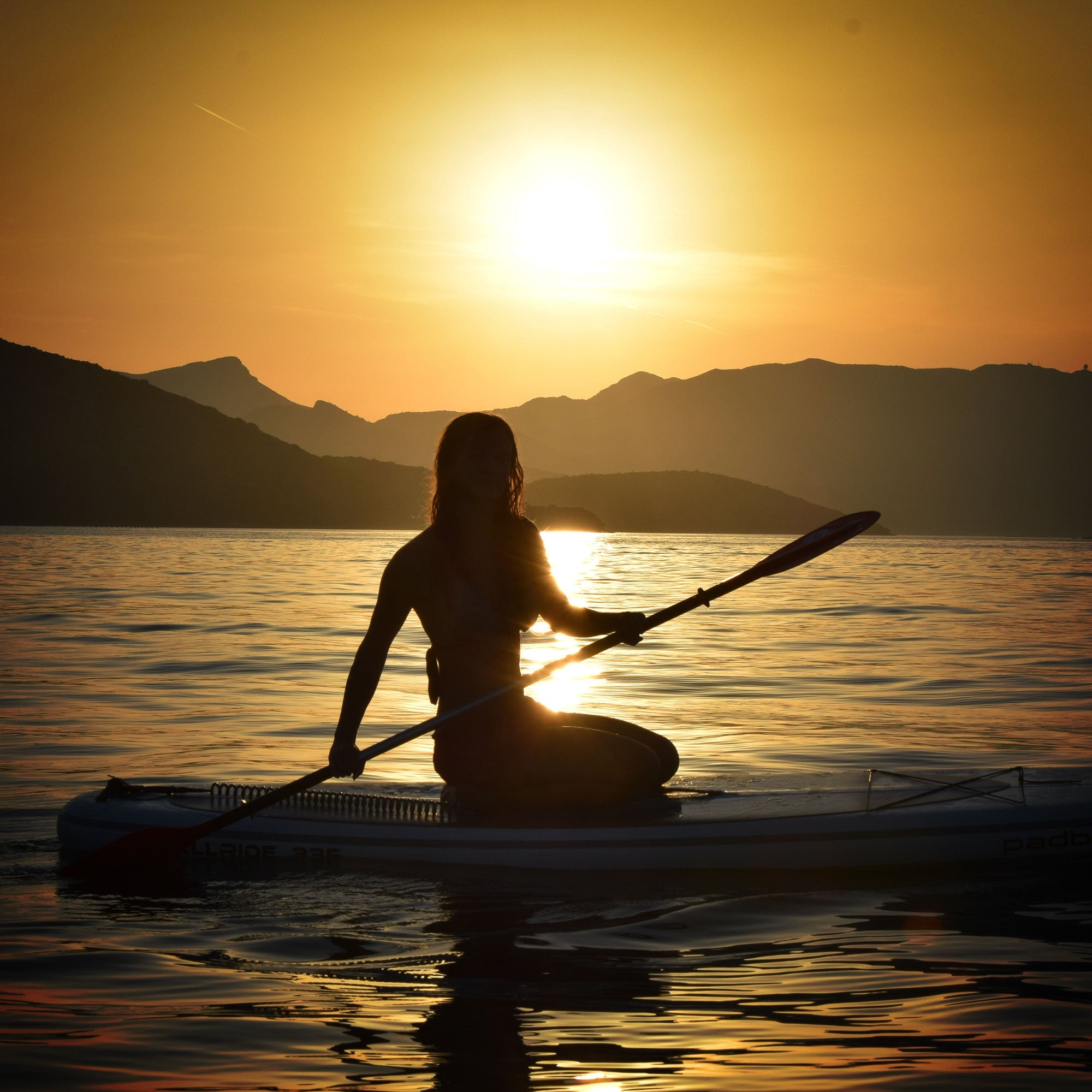 Silhouette einer Person auf einem Kajak bei Sonnenuntergang, Wasser im Vordergrund.