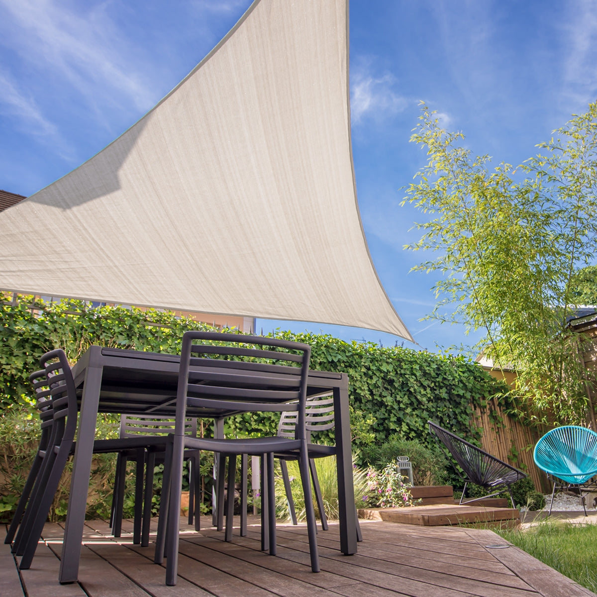 Jardín con una vela solar triangular color crema sobre una mesa y sillas.