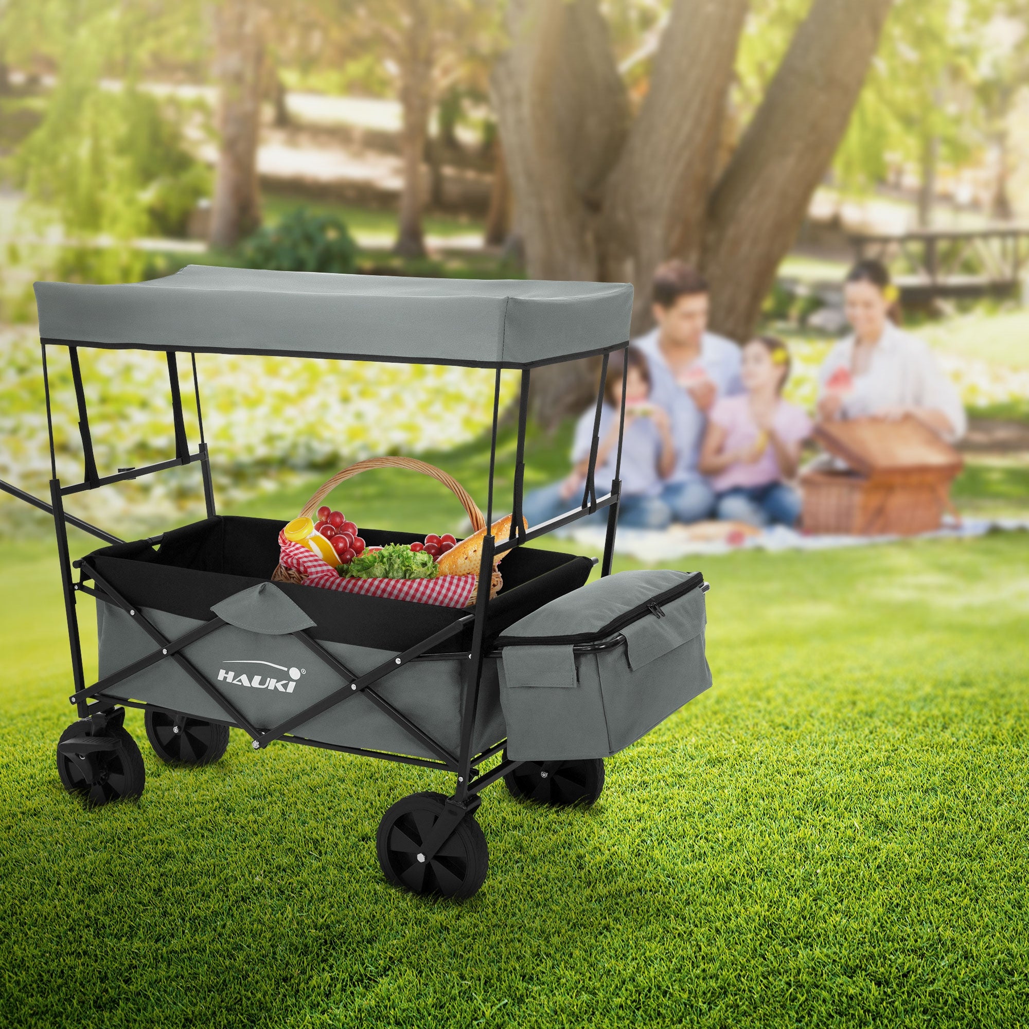 Ein Kinderwagen mit Obstkorb im Freien, Familienpicknick im Hintergrund.