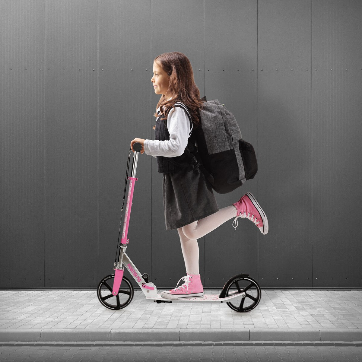 Ein Mädchen fährt auf einem pinken Cityroller auf einem Gehweg.