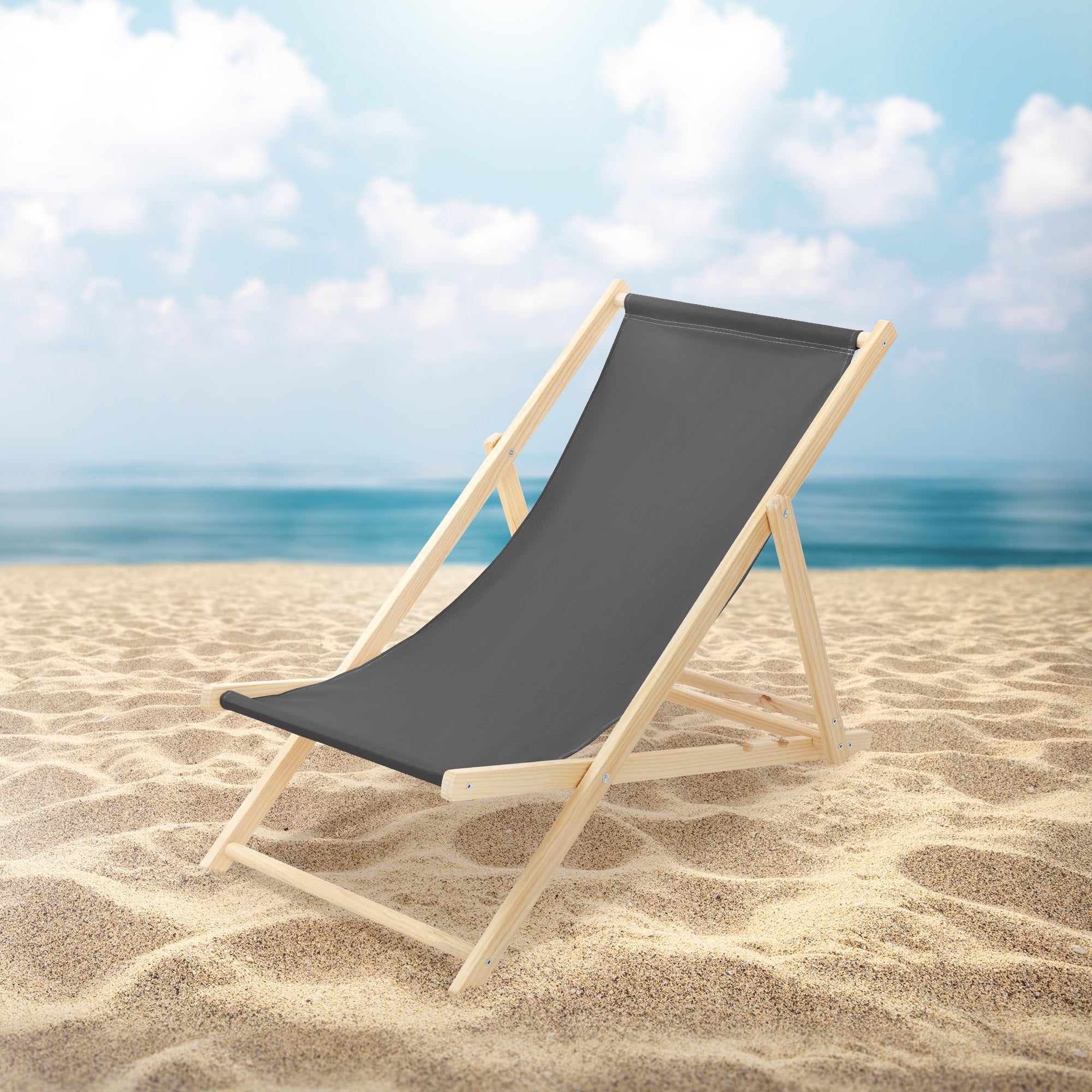 Grauer Liegestuhl auf einem Sandstrand mit Meer im Hintergrund.