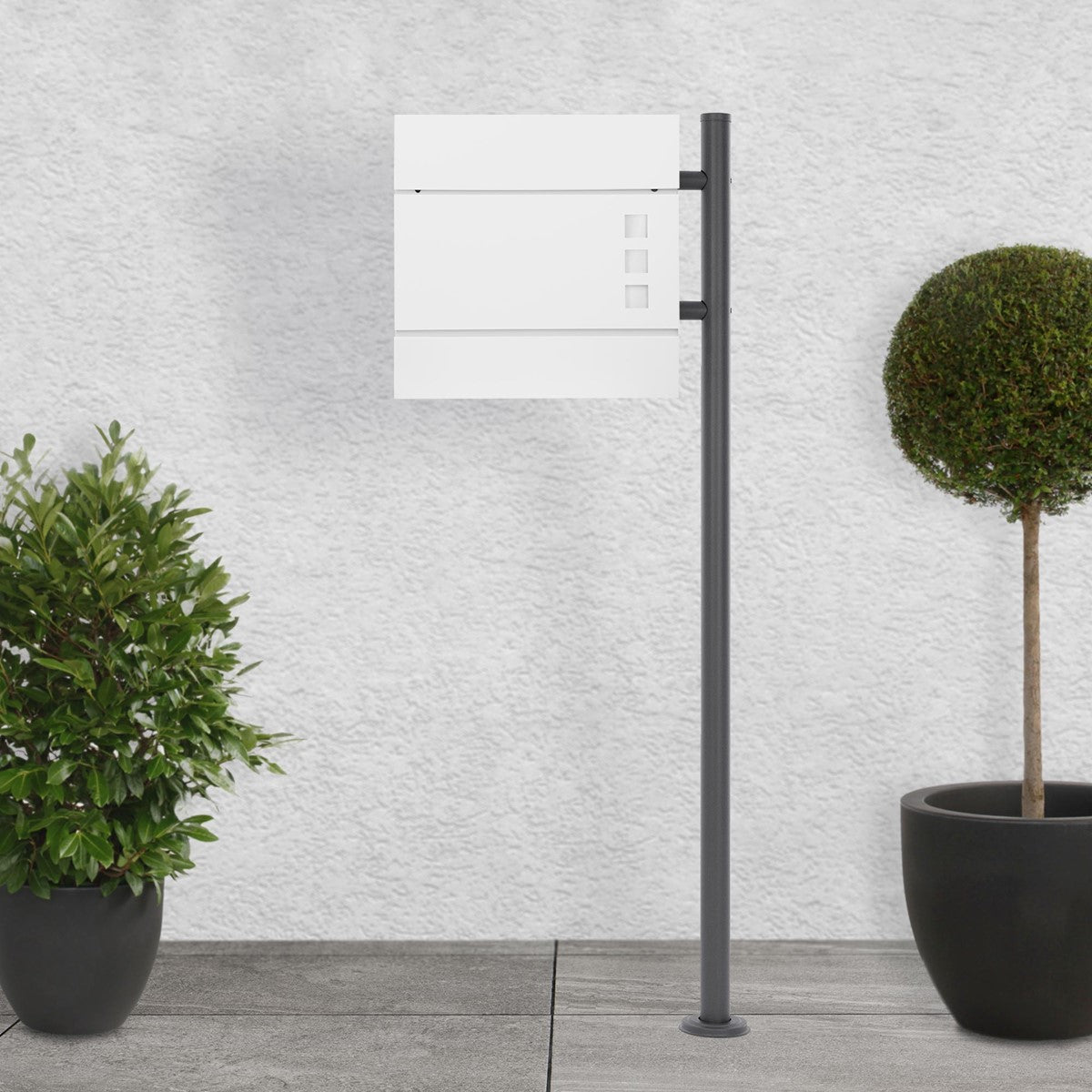 White mailbox on a gray base, surrounded by potted plants.