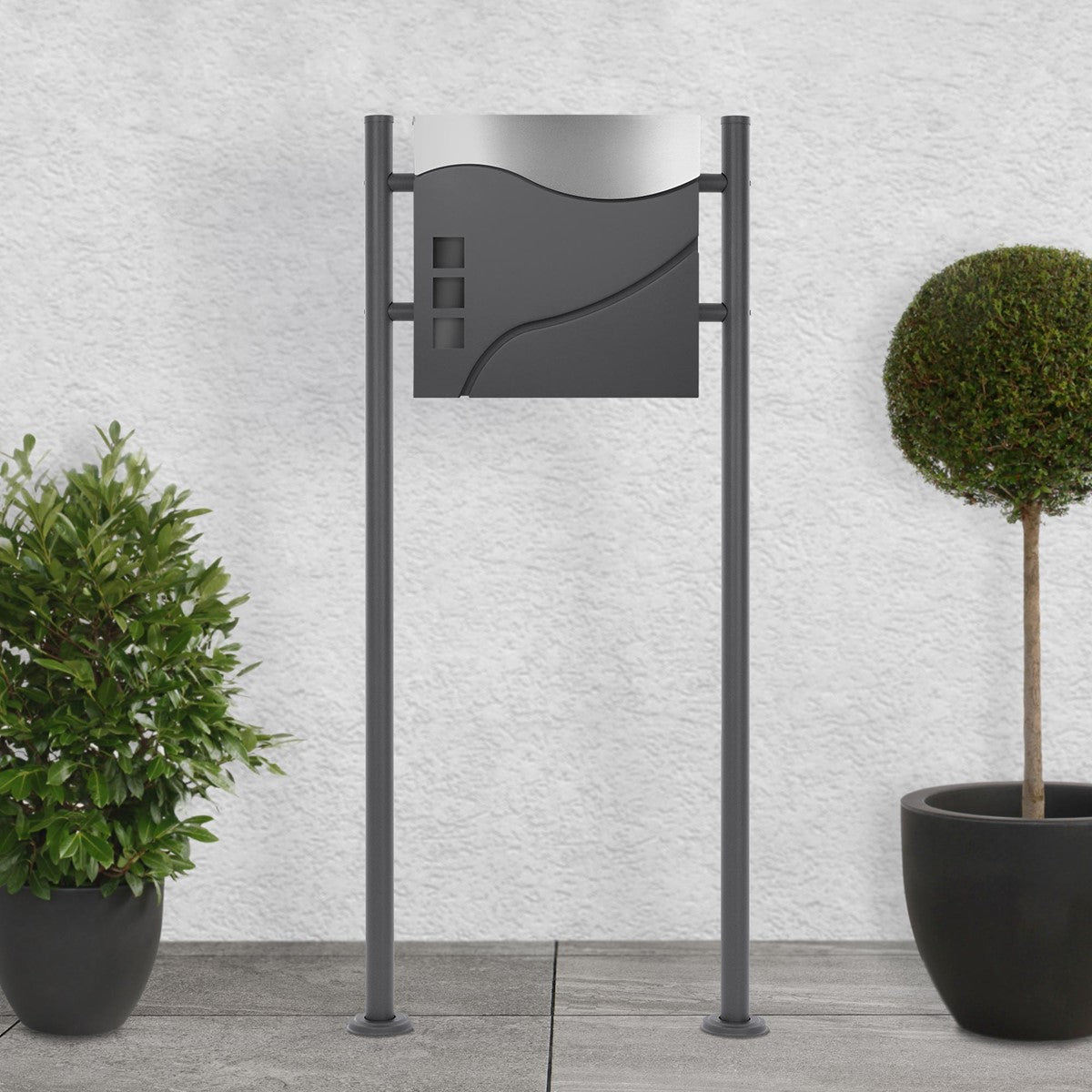 Letterbox on a stand, surrounded by two round plants.