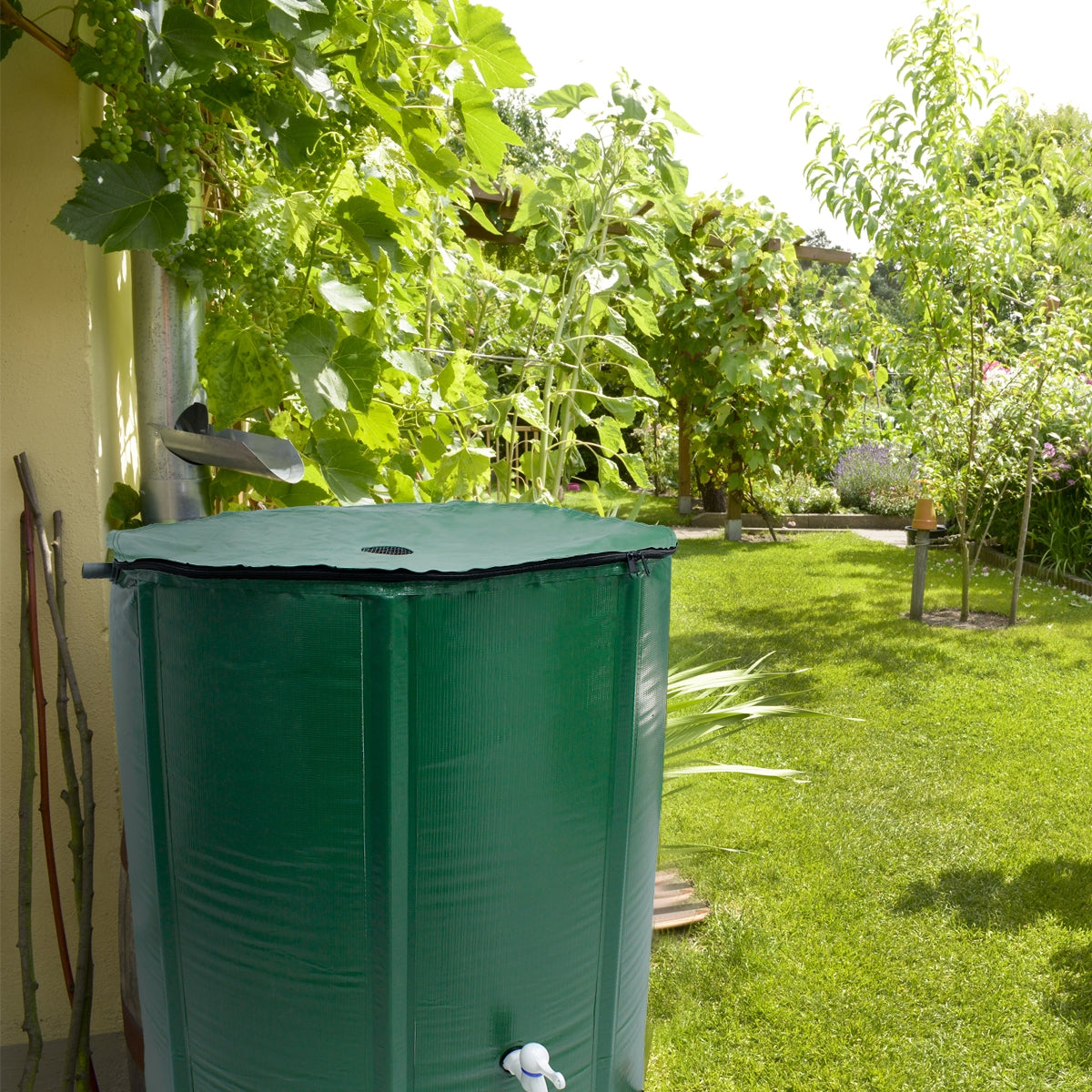 Grüner Wassertank im Garten, umgeben von Pflanzen und Bäumen.