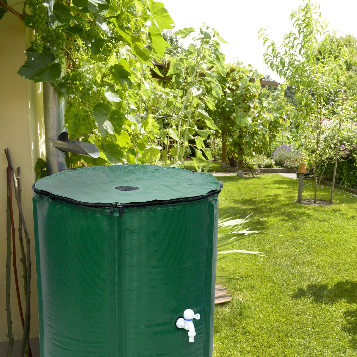 Grüner Wassertank im Garten, umgeben von Pflanzen und Rasen.
