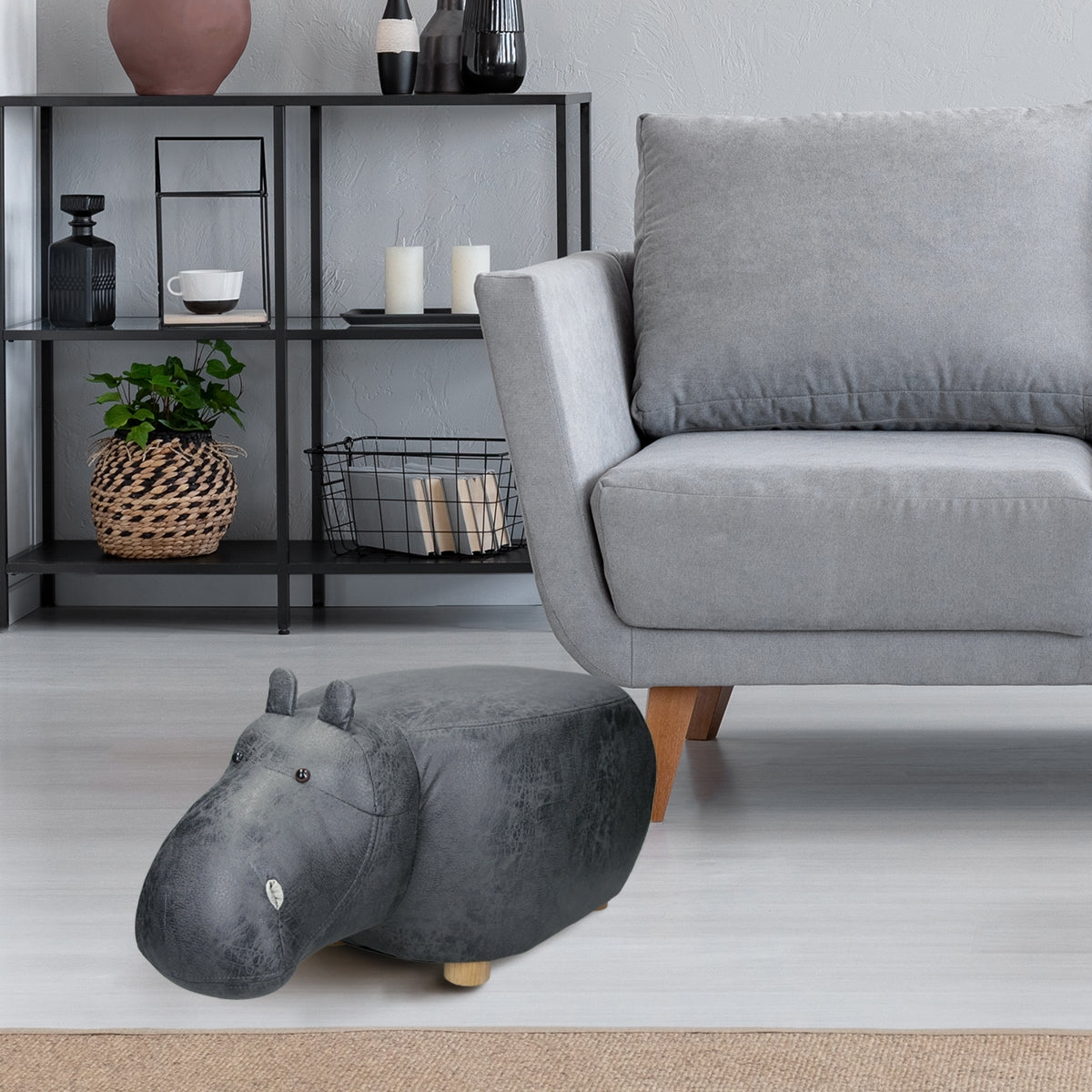 A gray hippopotamus stool in front of a modern sofa in a bright room.
