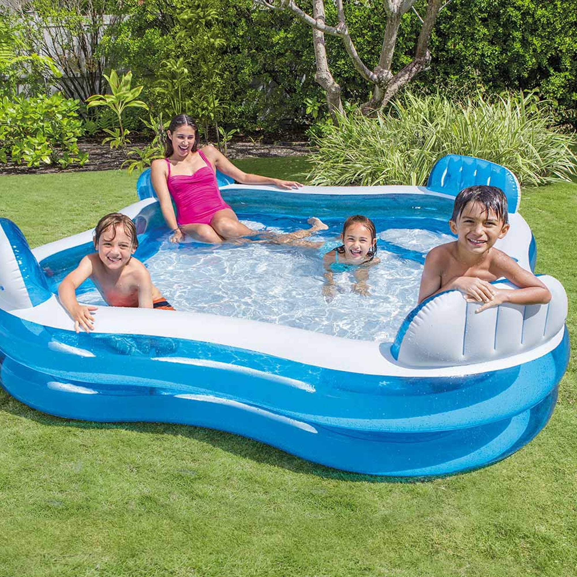 Des enfants et une femme jouent dans une grande piscine bleue dans le jardin.