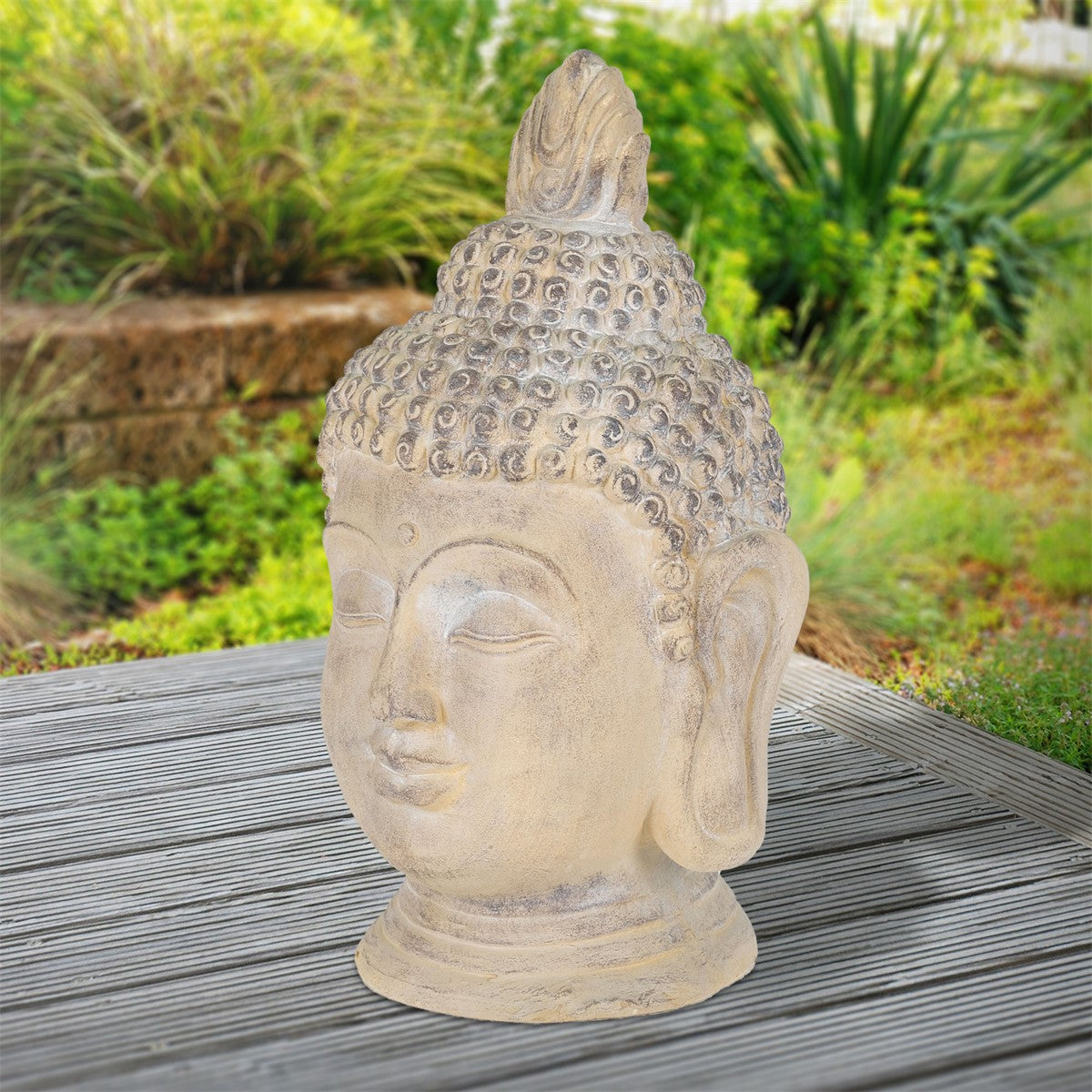 Buddha-Kopf aus Stein, auf einem Holztisch, umgeben von Pflanzen.