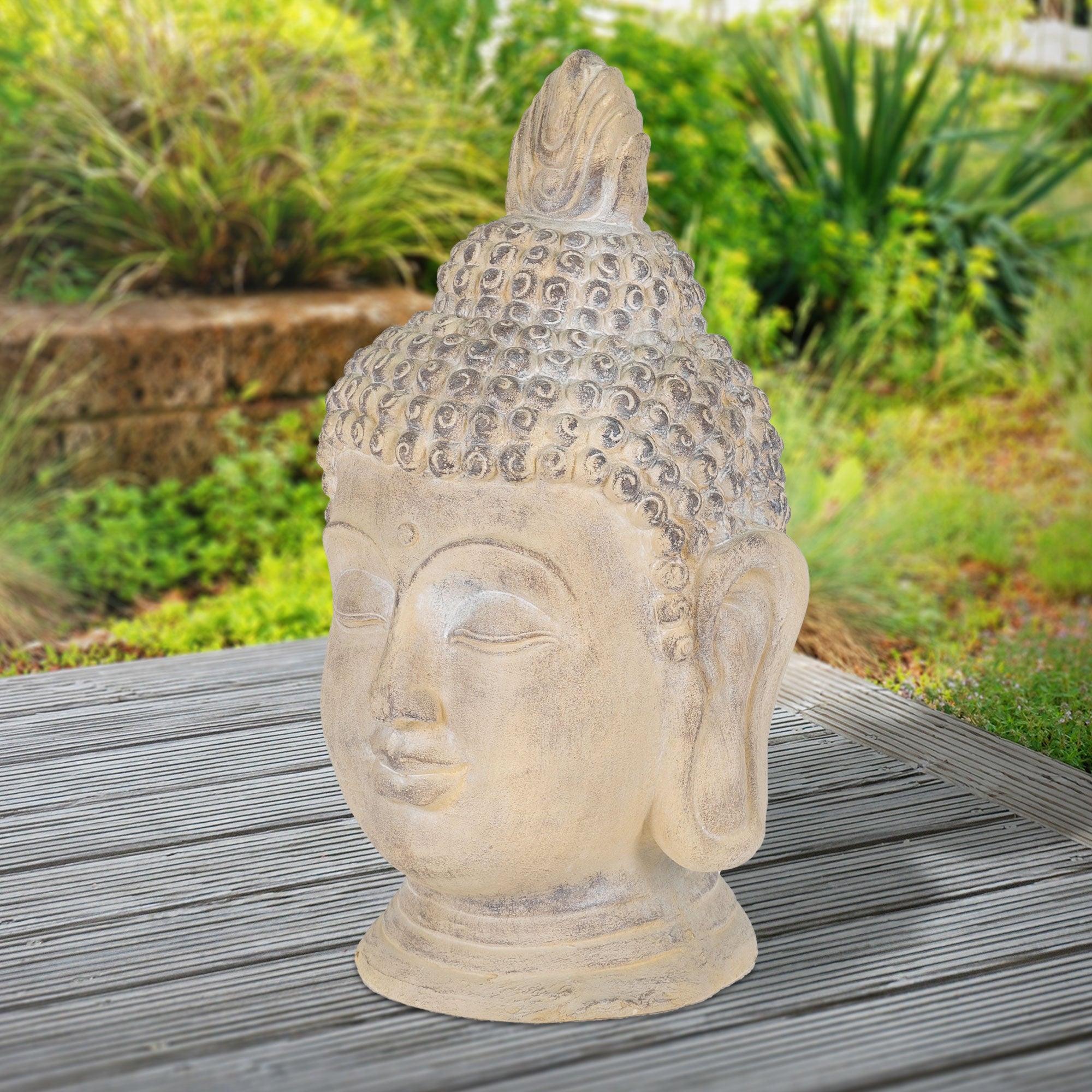 Buddha-Kopf aus Stein, auf einem Holztisch, umgeben von Pflanzen.