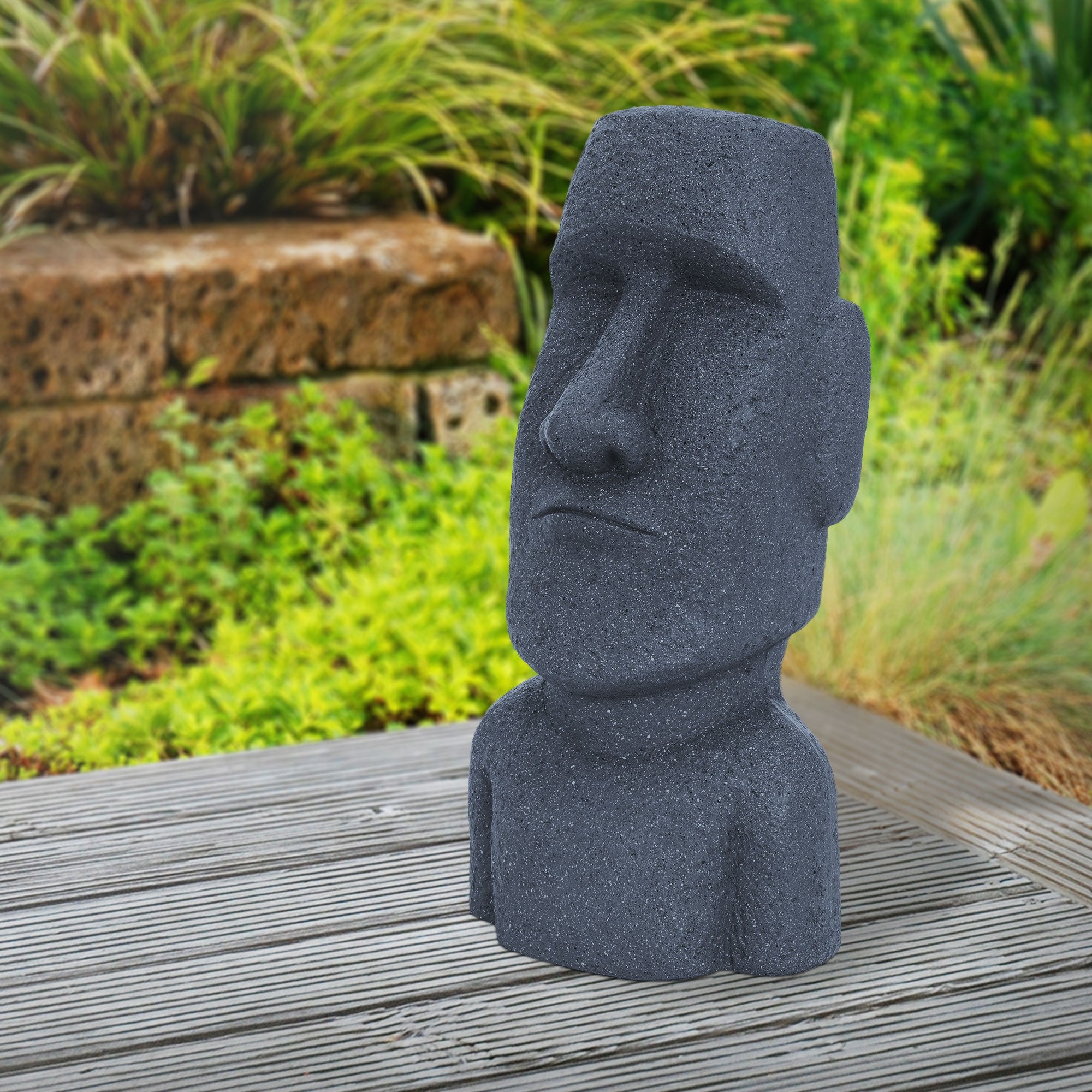 Moai Statue aus Stein, auf einem Tisch, mit grünen Pflanzen im Hintergrund.