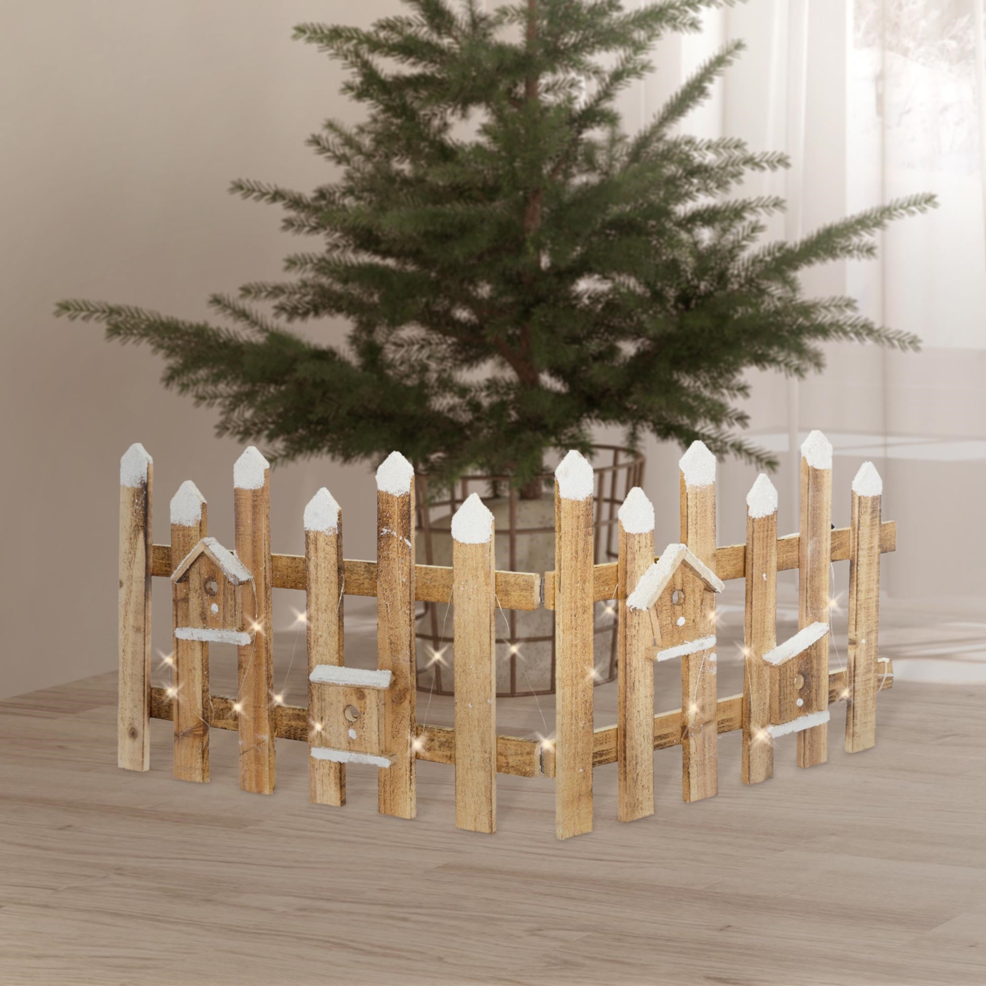Holzzaun mit weißen Spitzen vor einem Weihnachtsbaum in einem hellen Raum.