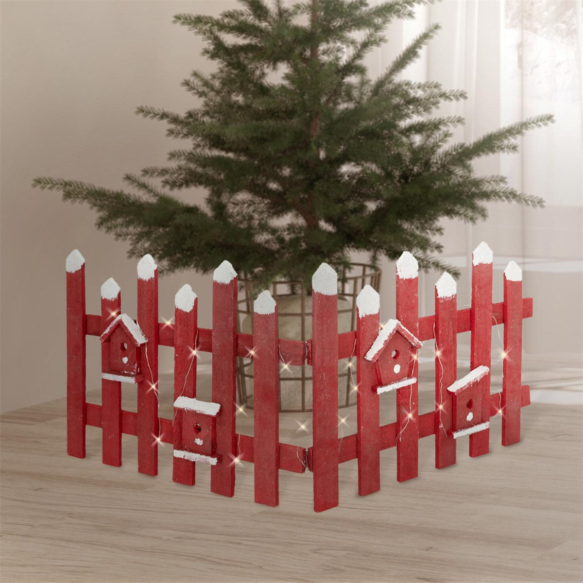 Roter Zaun mit weißen Spitzen und Vogelhäusern, um einen Weihnachtsbaum.