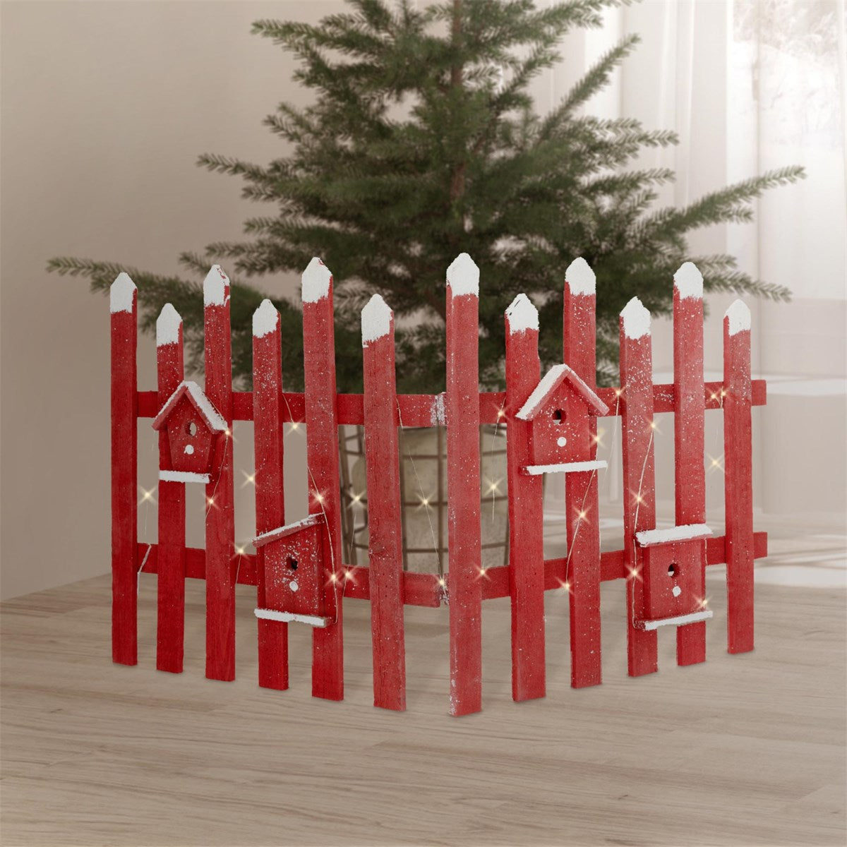 Ein roter Zaun mit Vogelhäusern und einem Weihnachtsbaum im Hintergrund.