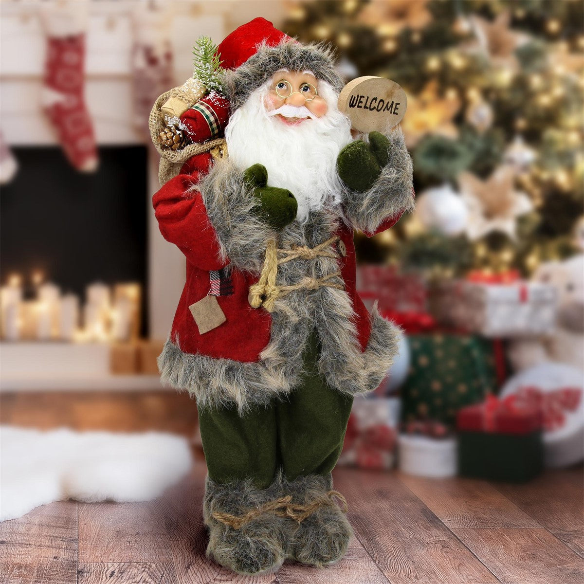 Santa Claus s vrecom a tabuľkou „WELCOME“ pred vianočným stromčekom.