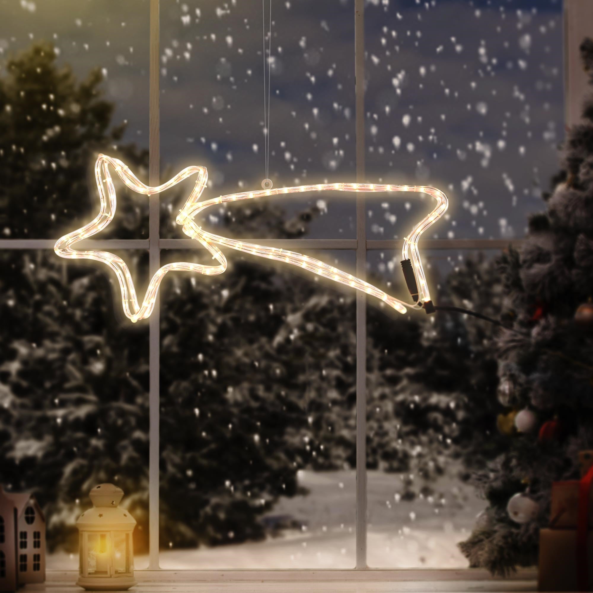 Leuchtender Stern mit Schweif vor einem Fenster, Weihnachtsbaum im Hintergrund.