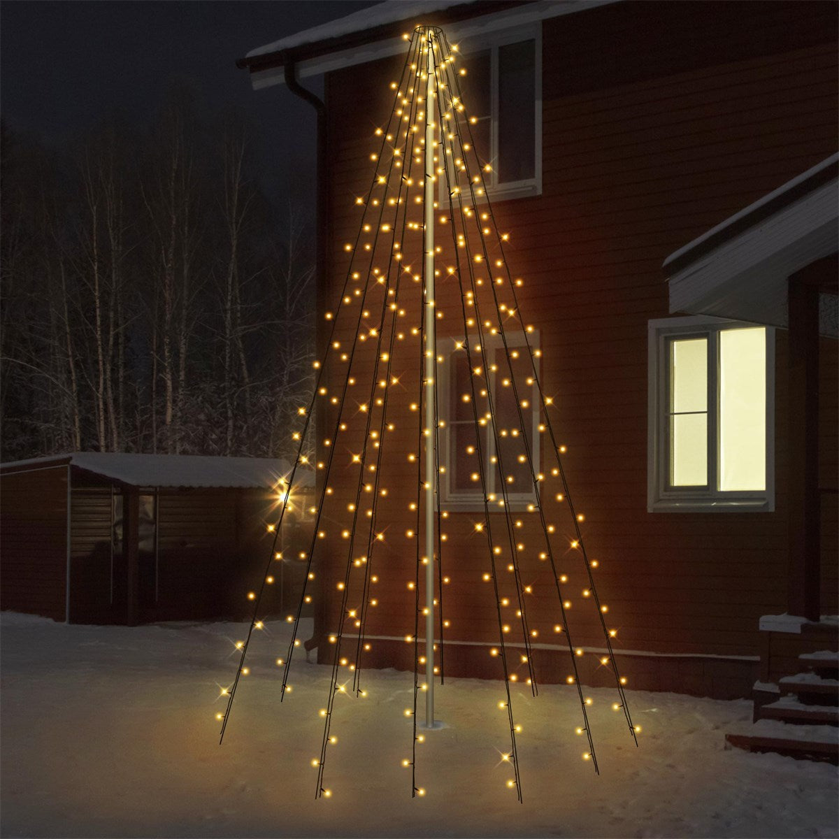 Et oplyst juletræ foran et hus om natten.