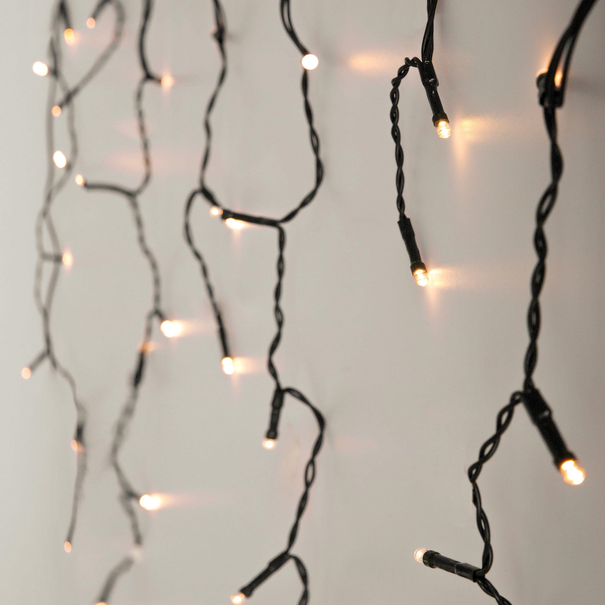 Lichterkette mit kleinen, leuchtenden Lampen an einem weißen Hintergrund.