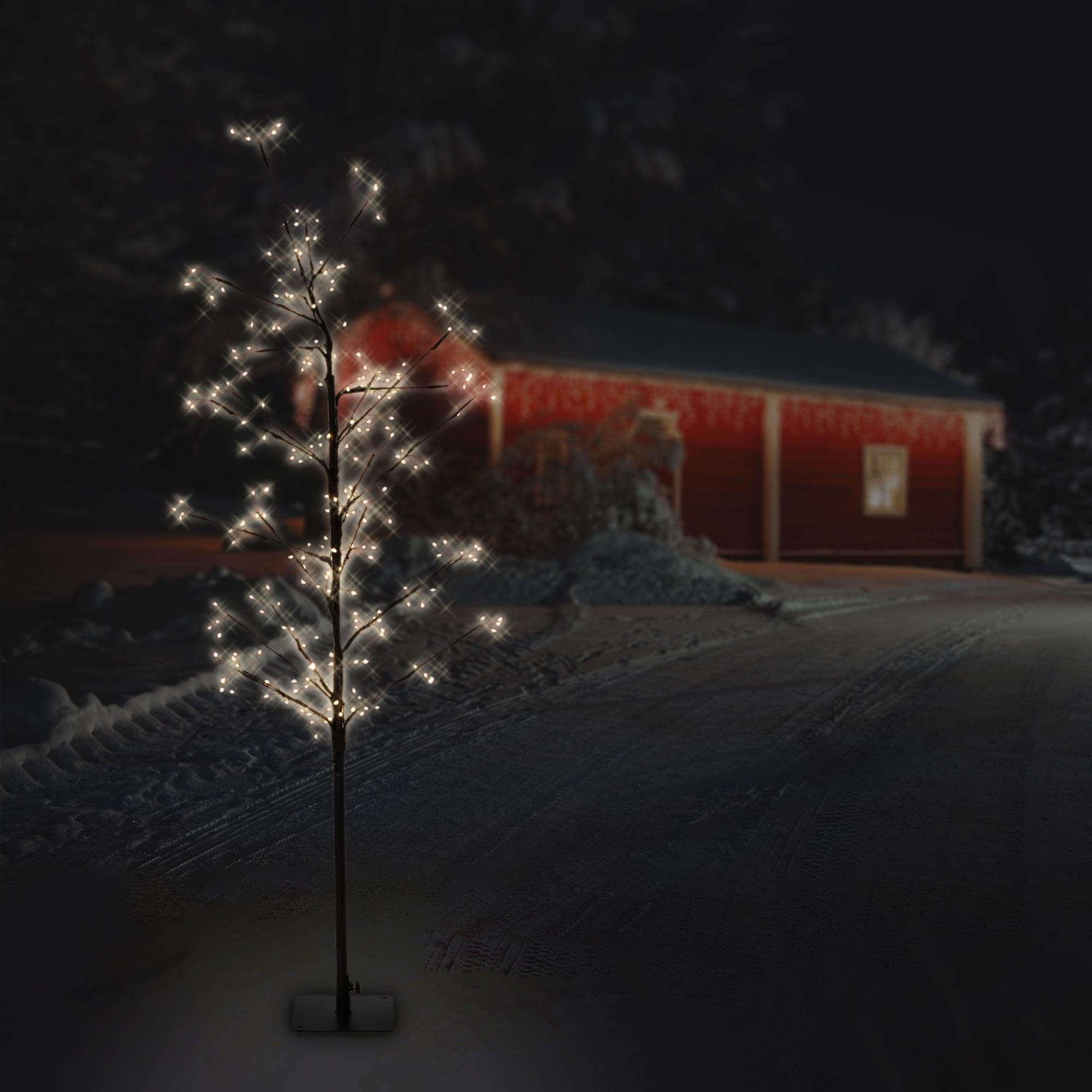 Árbol artificial iluminado frente a un edificio rojo por la noche.