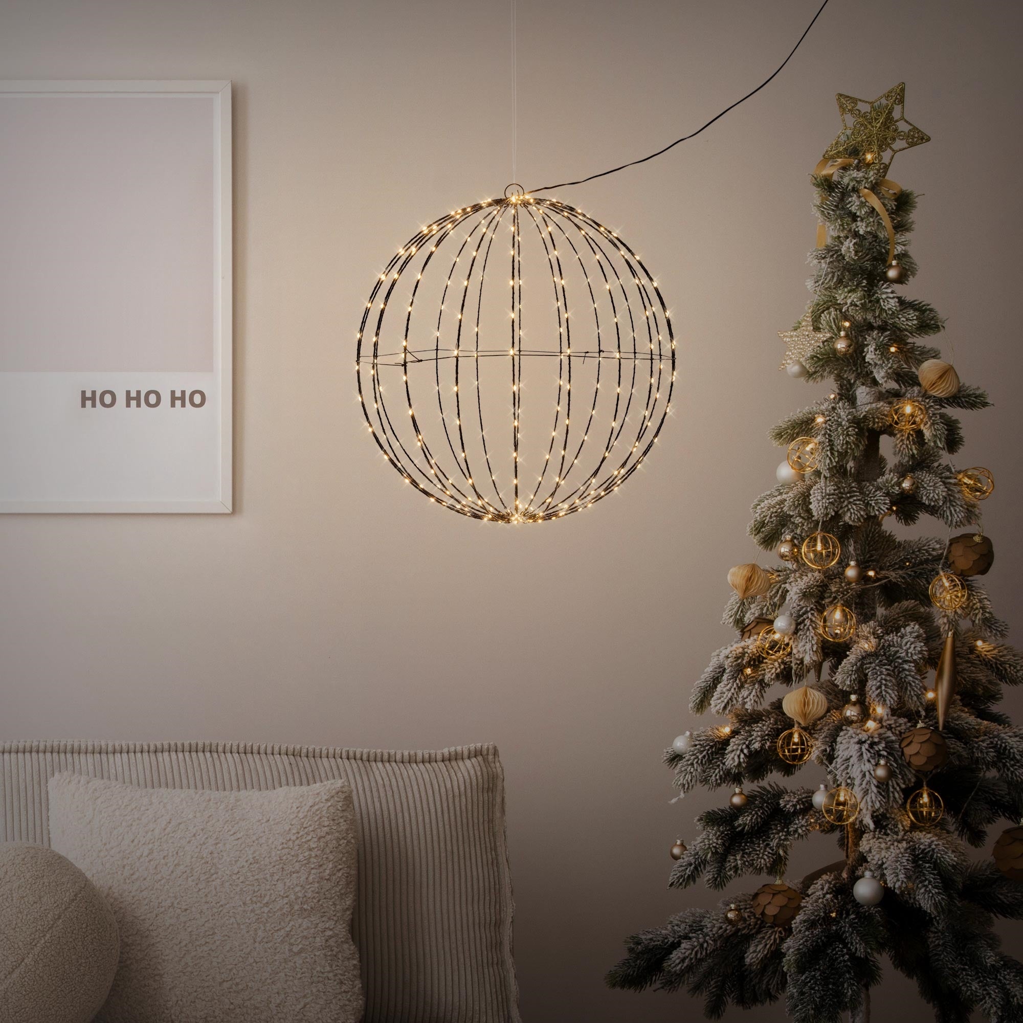 A round, illuminated decoration hangs over a Christmas tree.