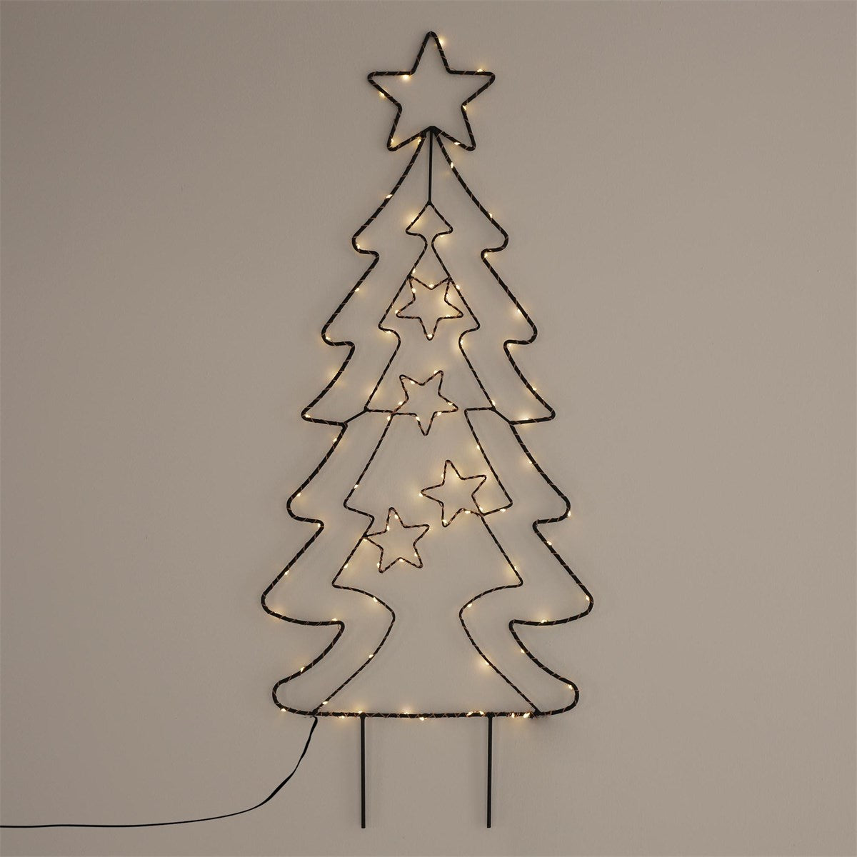Drahtbaum mit Lichtern, geformt wie ein Weihnachtsbaum, an einer Wand.