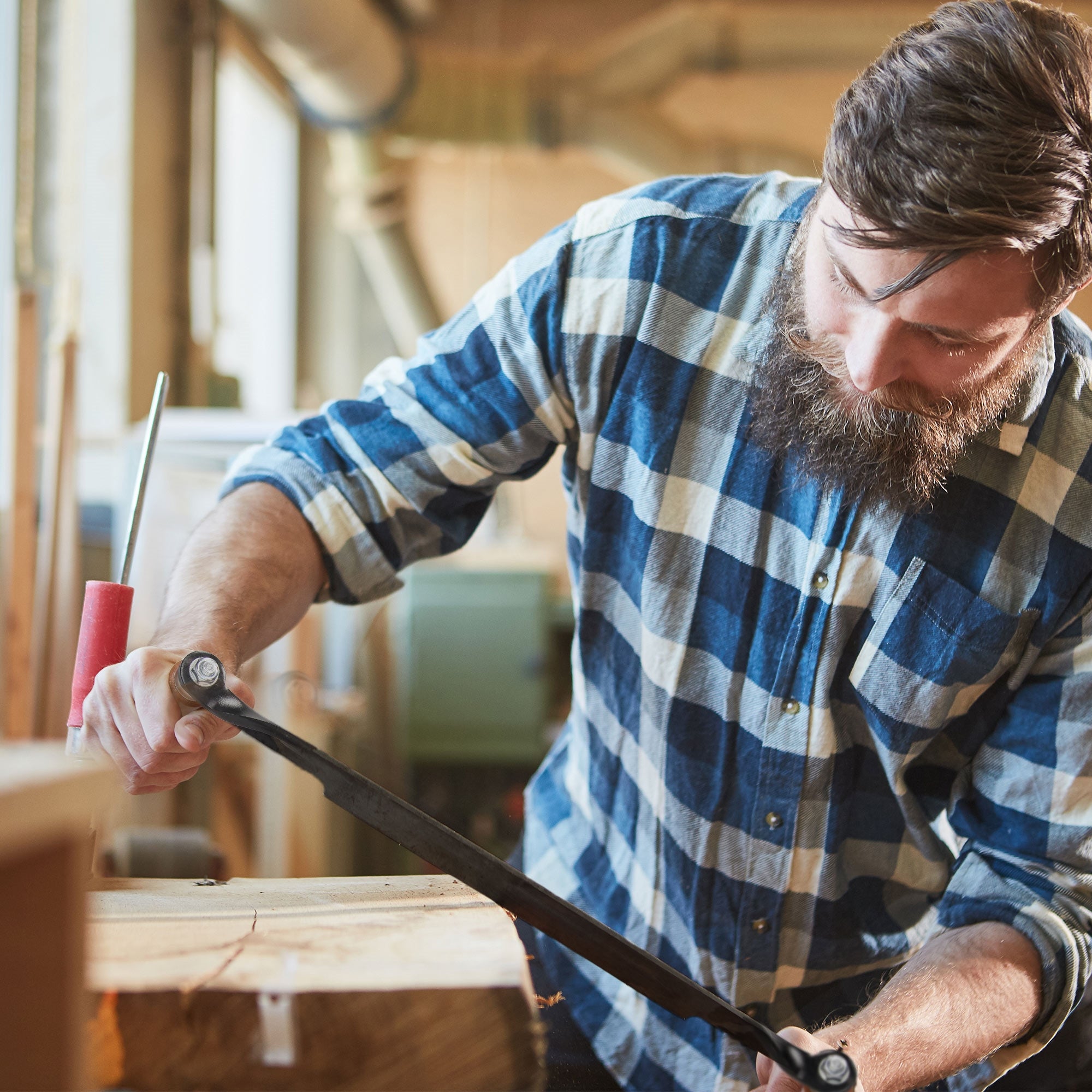 Un hombre con barba trabaja en un trozo de madera en un taller.