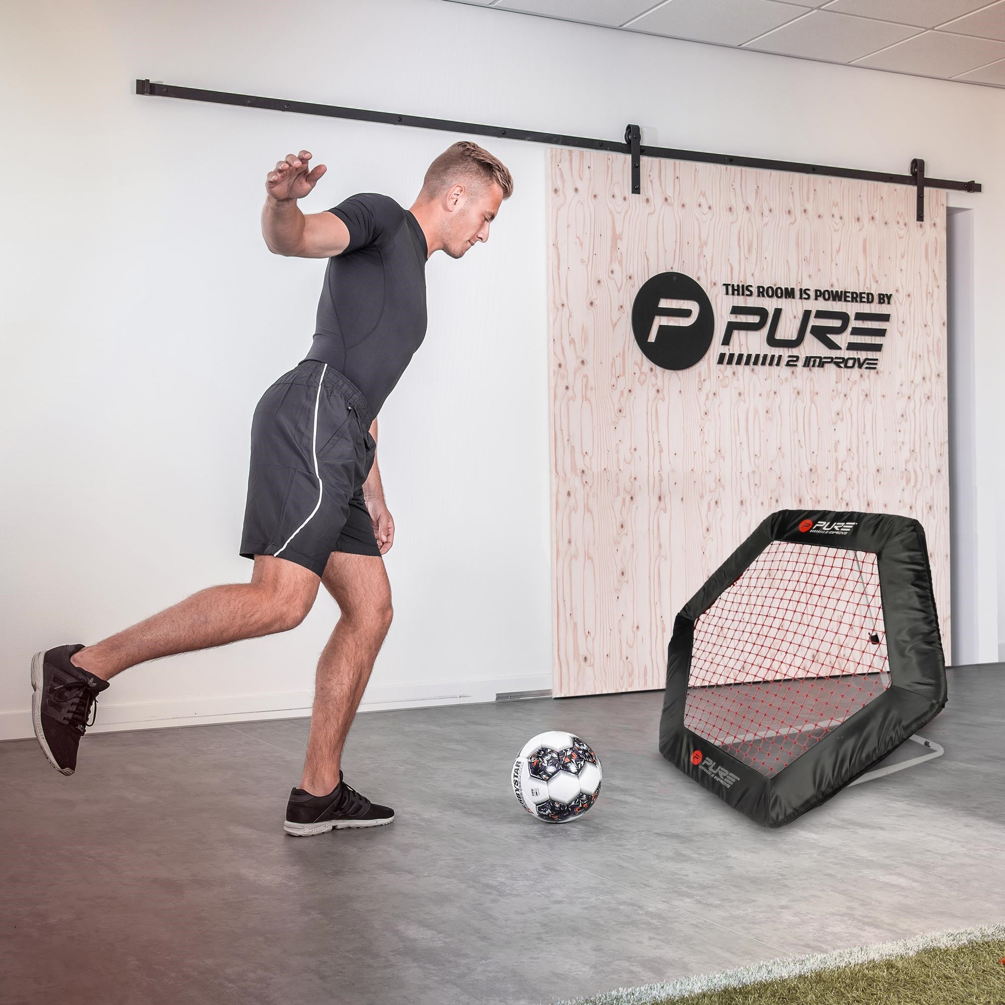 Mann, der auf einen Fußball schießt, mit einem Rebounder im Hintergrund.