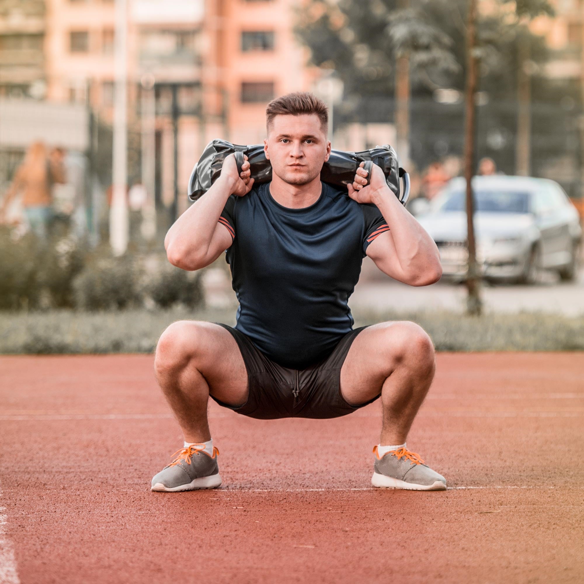 Muž ve sportovním oblečení dělá dřep s Powerbagem na ramenou.