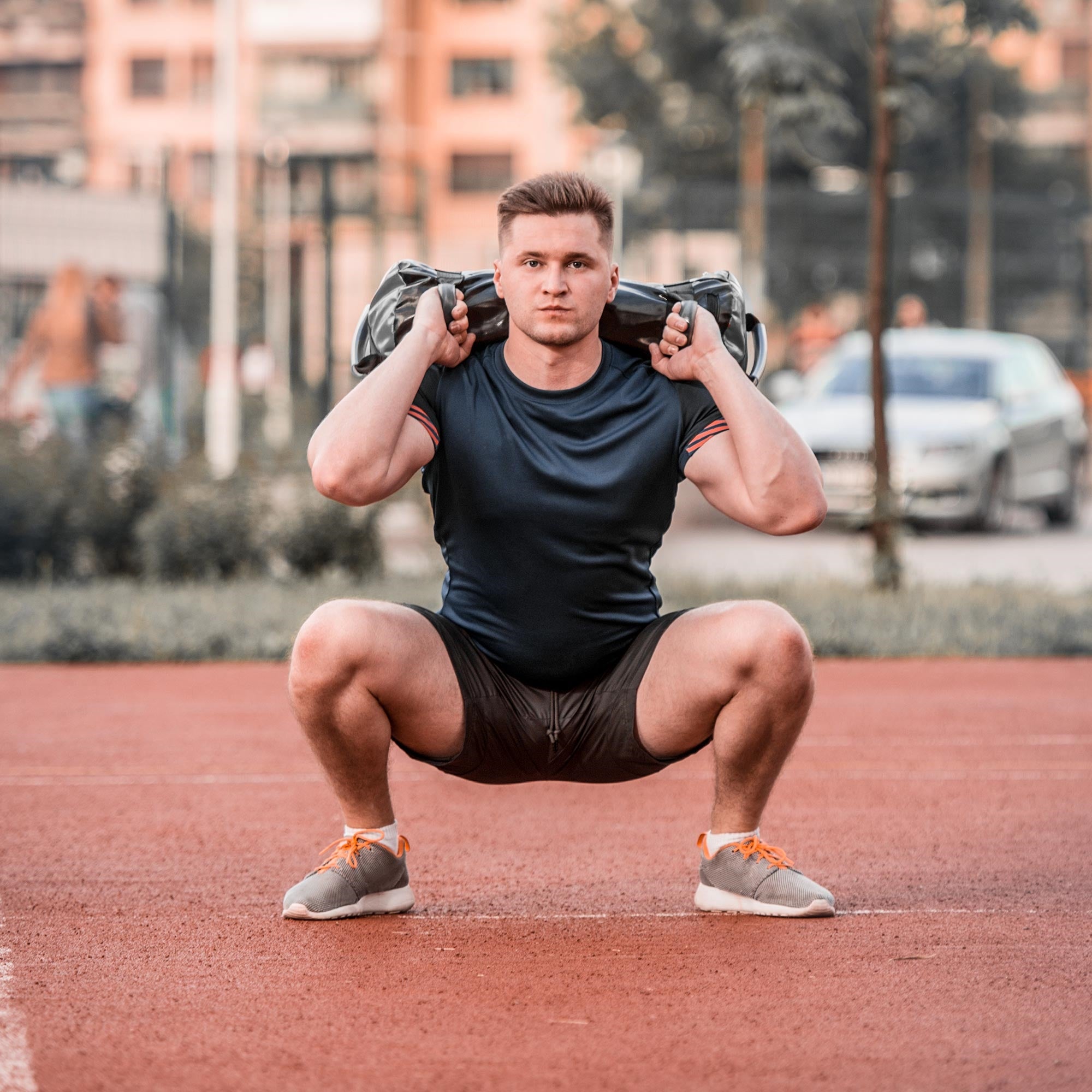 Muž ve sportovním oblečení dělá dřep s váhou na ramenou.