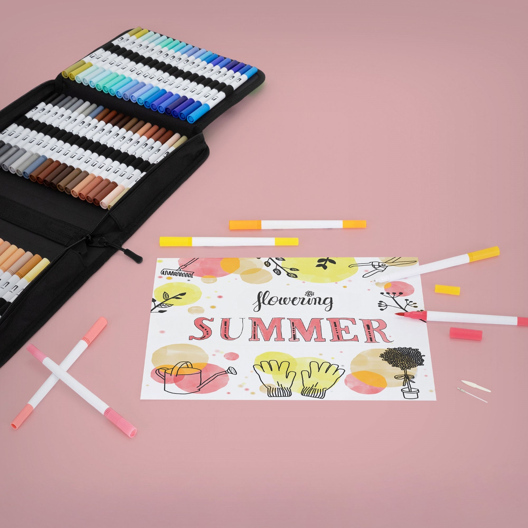 Colorful markers and a sheet with the text 'Flowering SUMMER' on a pink background.