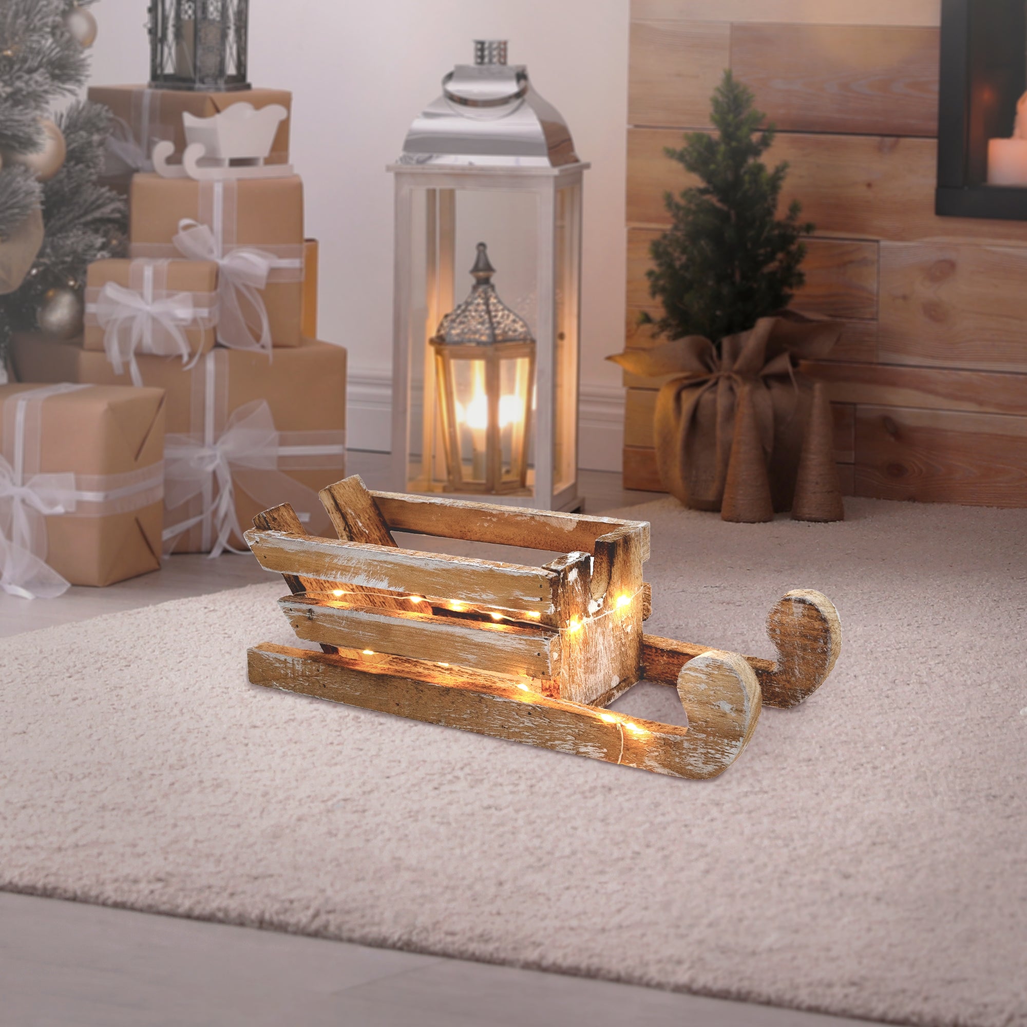 Trineo de madera con luces, sobre una alfombra, junto a una linterna y un árbol de Navidad.