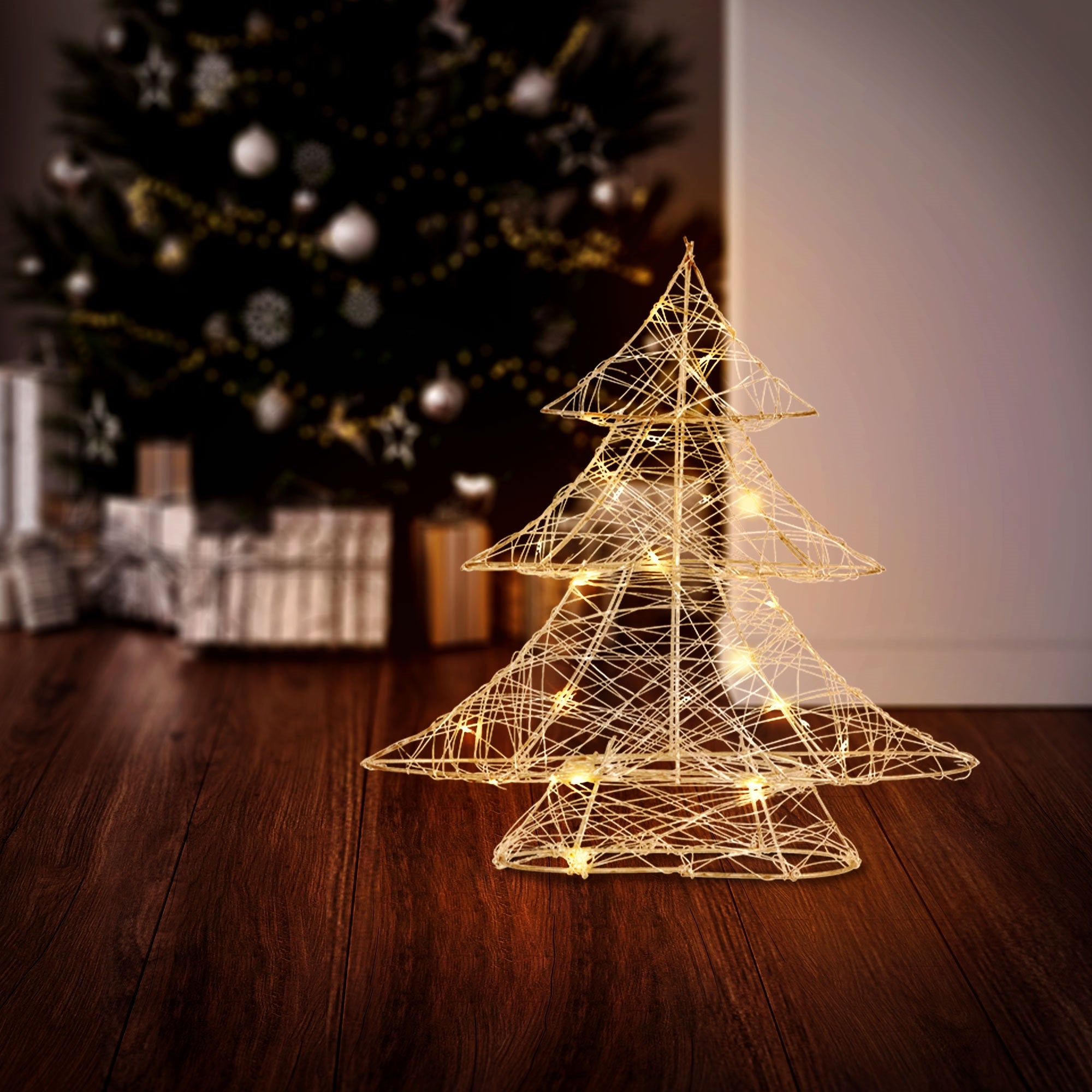 Ein beleuchteter Weihnachtsbaum aus Draht steht auf einem Holzboden vor einem Weihnachtsbaum.