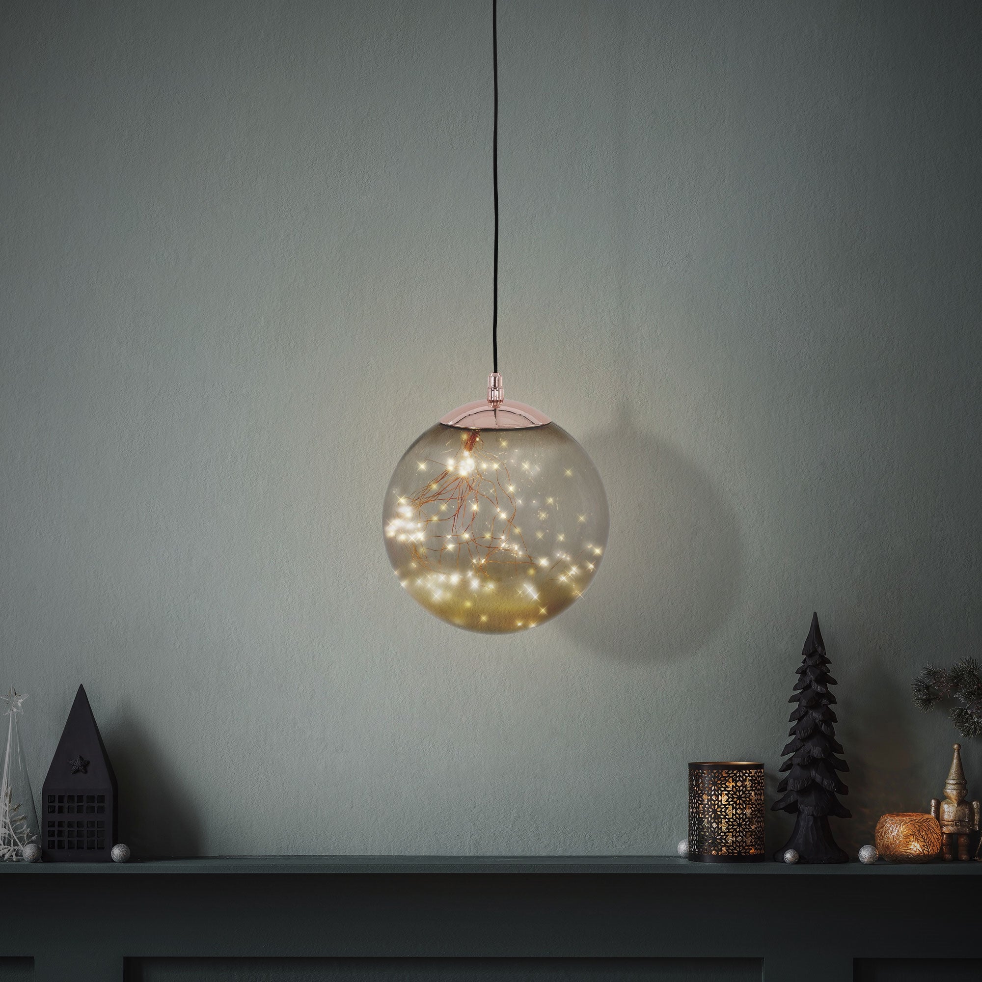 Hängende Glaskugel mit Lichtern, vor einer grauen Wand und Dekoration.