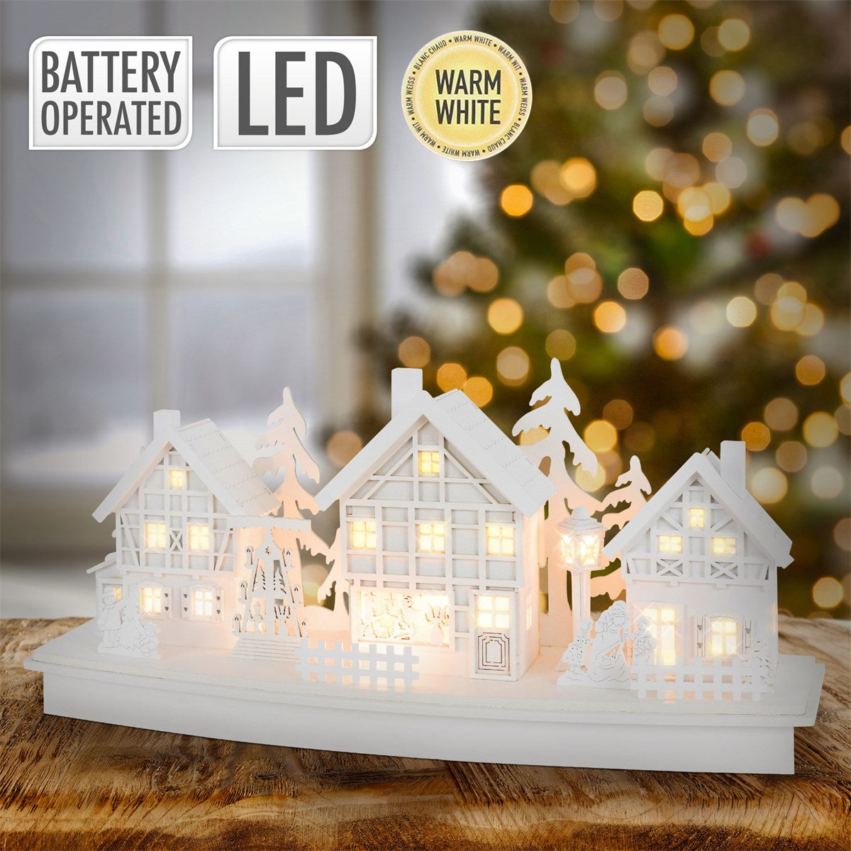 Dekorative LED-Lichterhäuser in weiß, vor unscharfem Weihnachtsbaum.