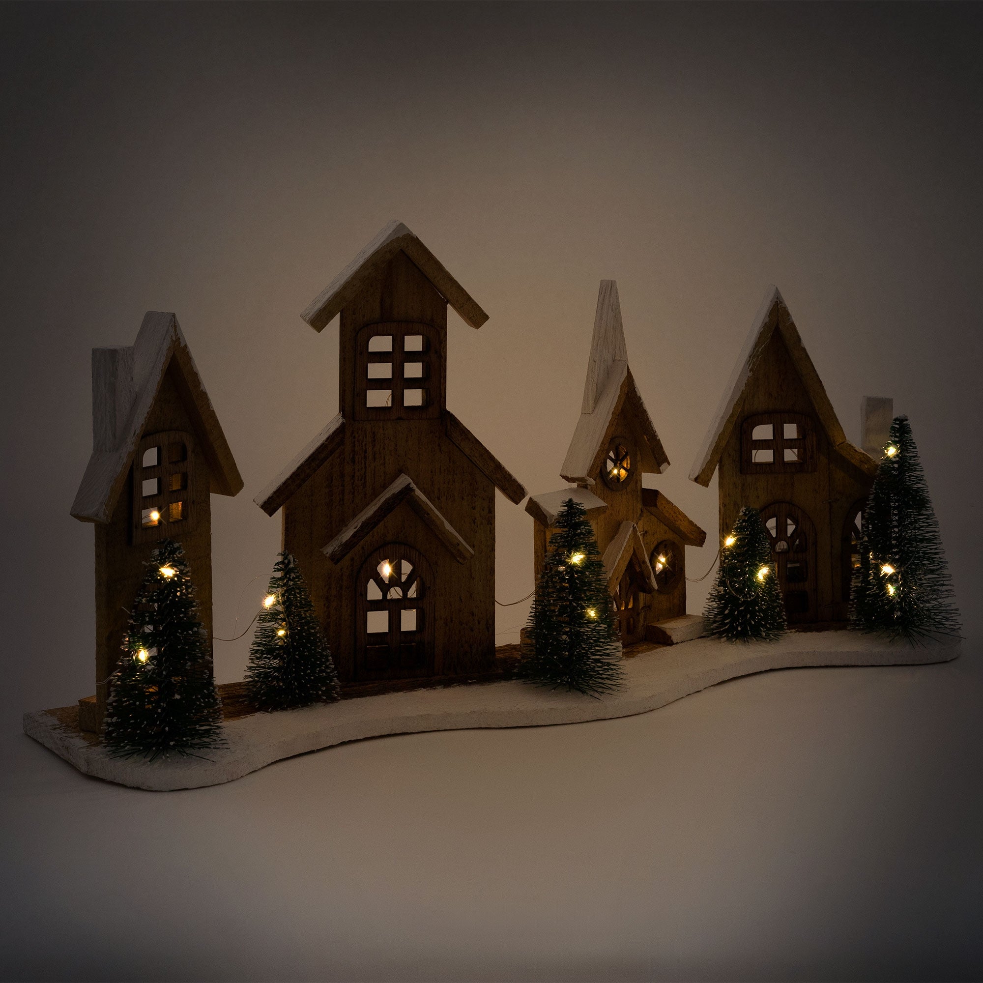 Decorative wooden houses with lights and small fir trees on a snowy landscape.