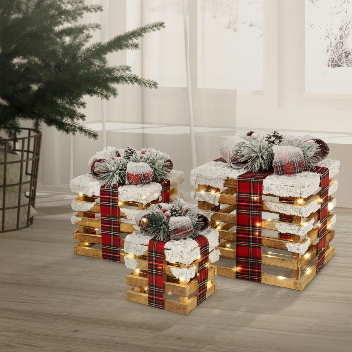 Drei gestapelte Holzkisten als Geschenke, mit roten Karobändern, Tannenzweigen und warmweißen Lichtern dekoriert.