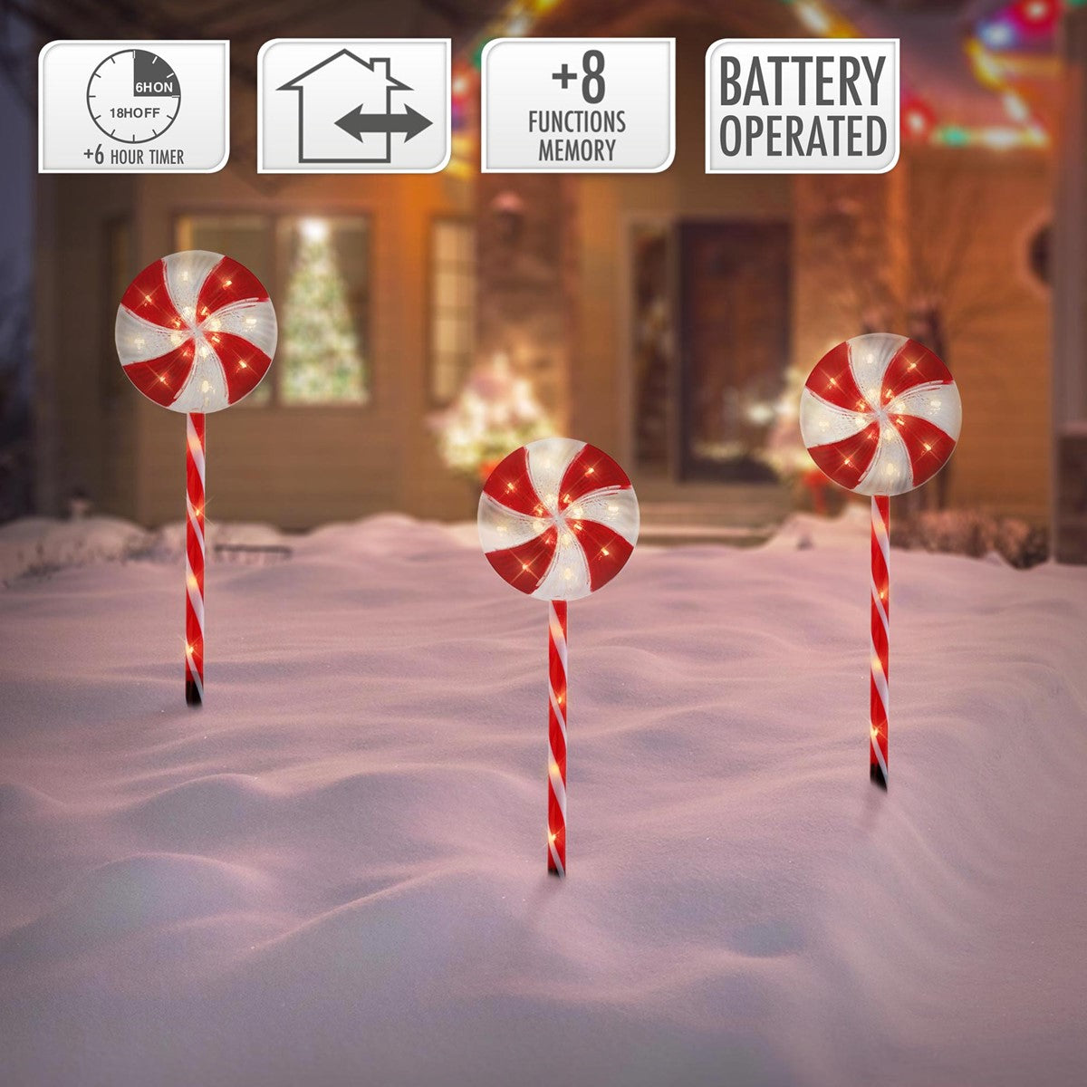 Drei leuchtende Zuckerstangen stehen im Schnee vor einem Haus.