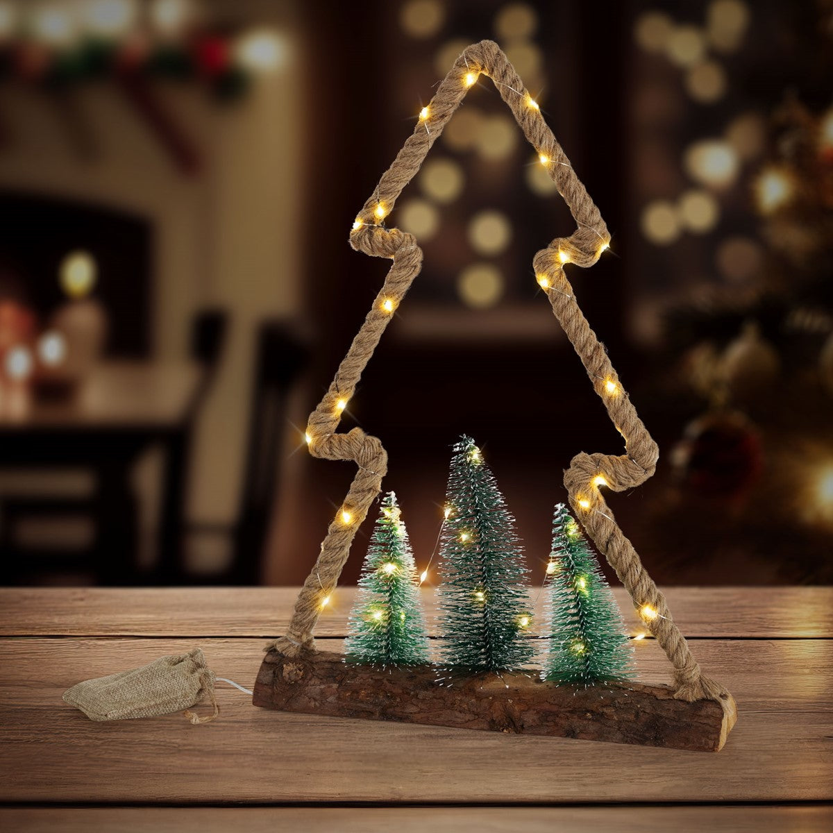 Beleuchteter Weihnachtsbaum aus Seil auf einem Holzsockel, davor stehen drei kleine Tannen.