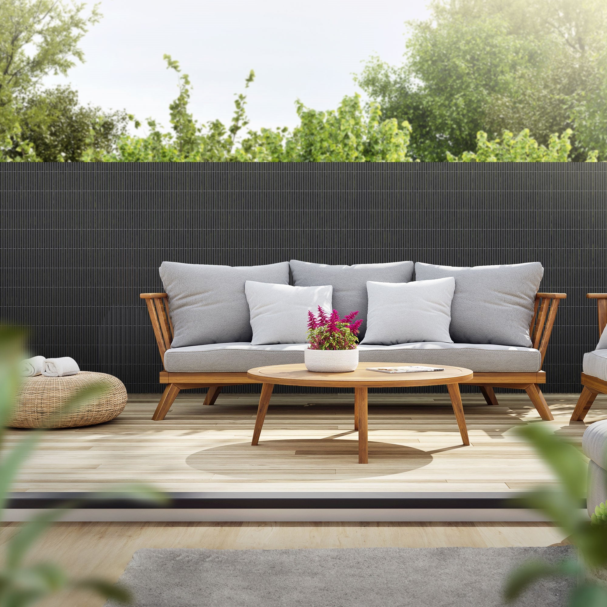 Gemütliche Terrasse mit Sofa, Tisch und Pflanzen im Hintergrund.