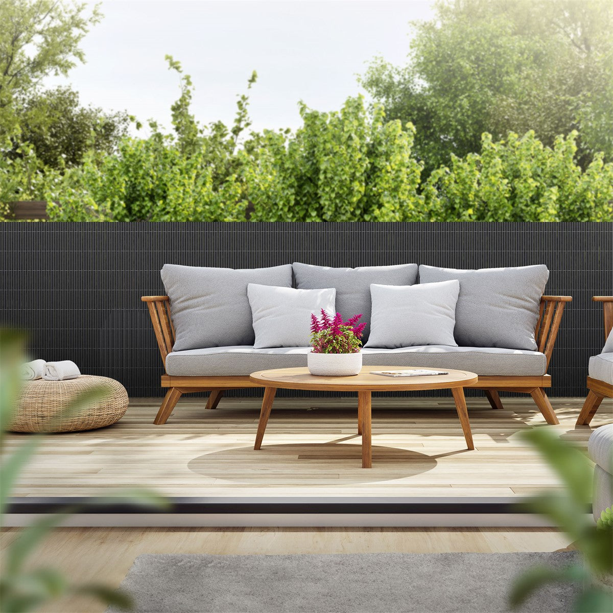 Gemütliche Sitzecke mit grauem Sofa, runden Tisch und Pflanzen im Hintergrund.