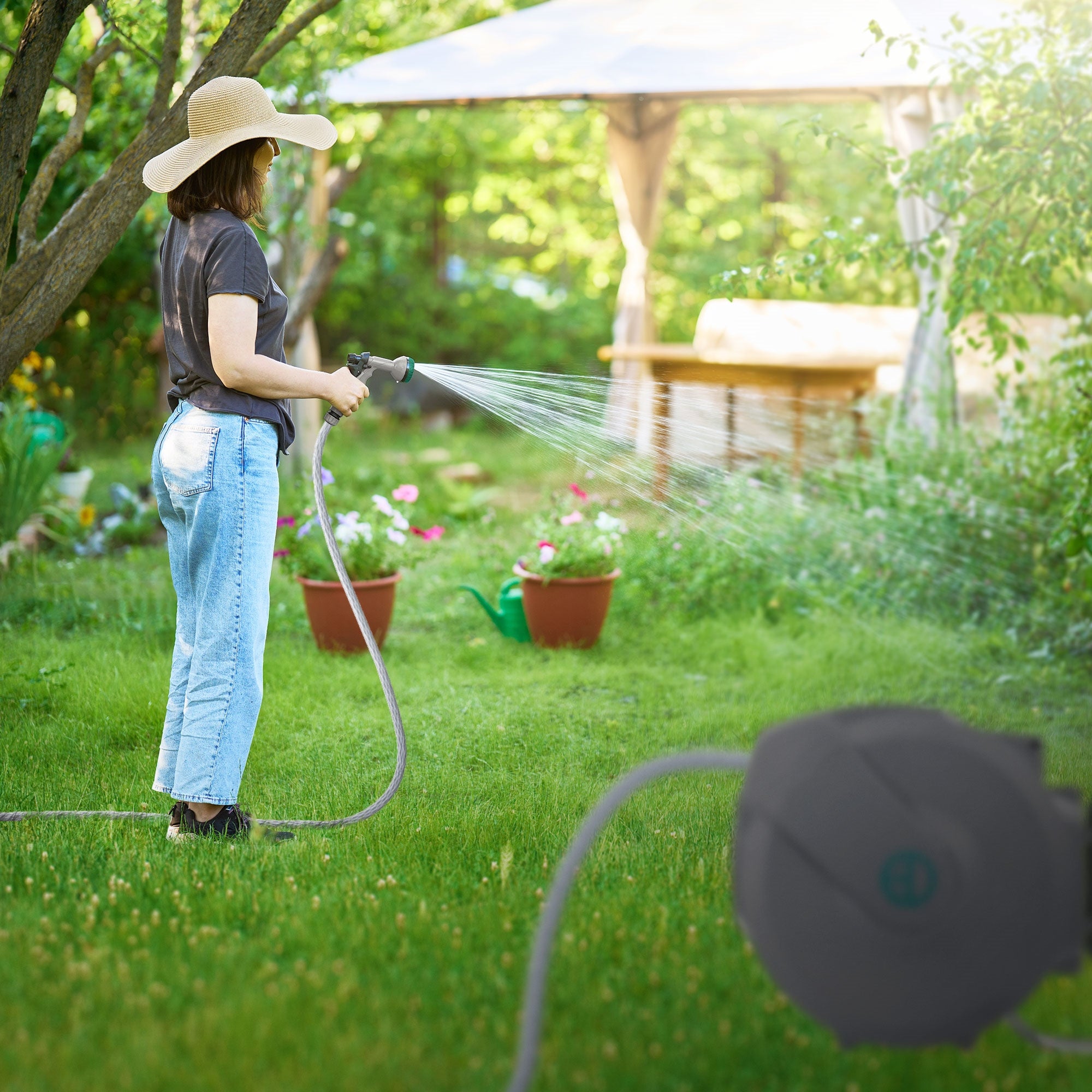 Frau im Garten mit Schlauch, spritzt Wasser auf Pflanzen.