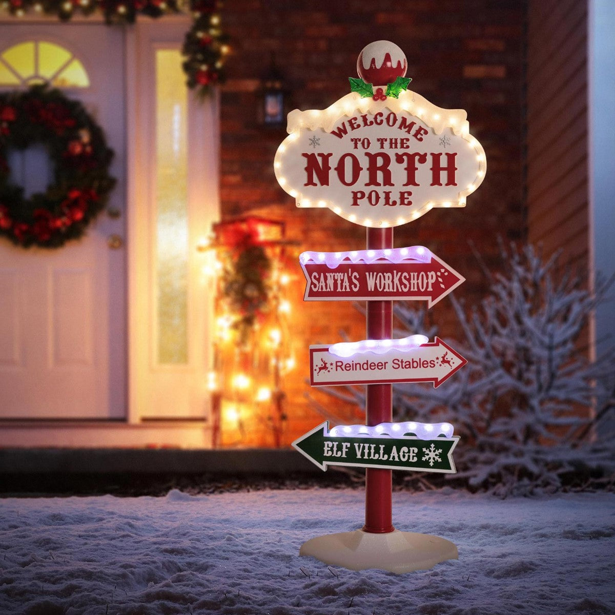 Leuchtendes Schild mit Richtungspfeilen zu Santa's Werkstatt und anderen Orten, vor einem festlich deko