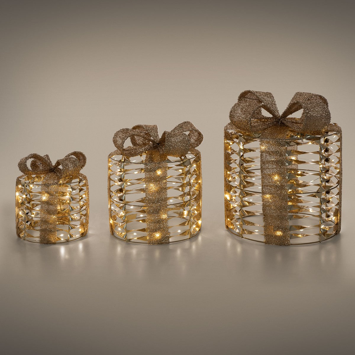 Drei Geschenke mit goldenen Schleifen und Lichtern auf einem grauen Hintergrund.