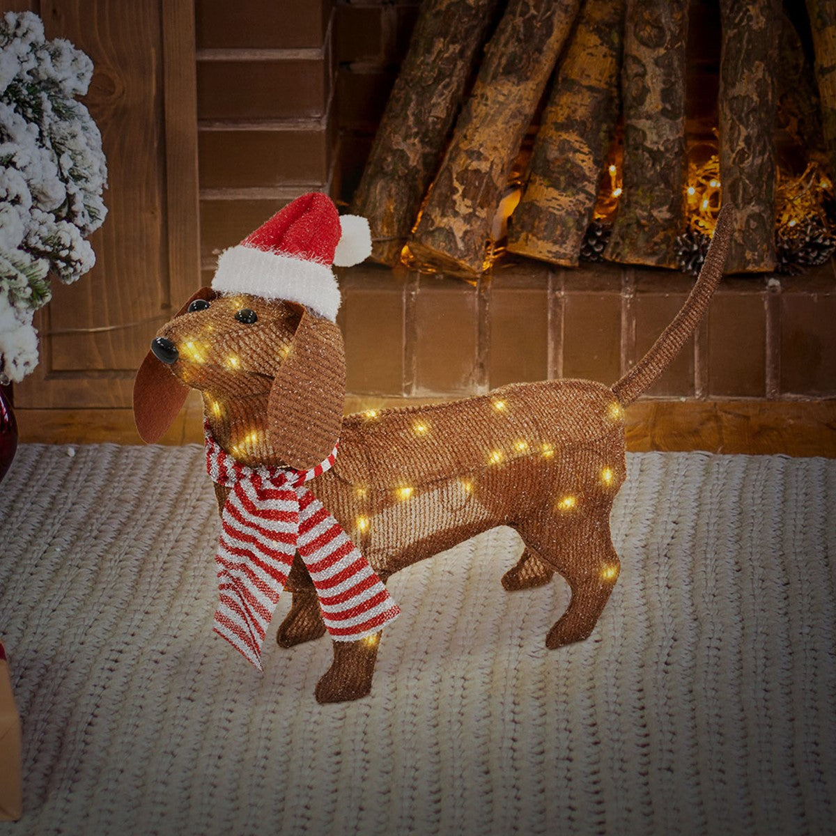 Ein dekorativer Hund aus Jute mit Weihnachtsmütze und Lichtern steht vor einem Kamin.