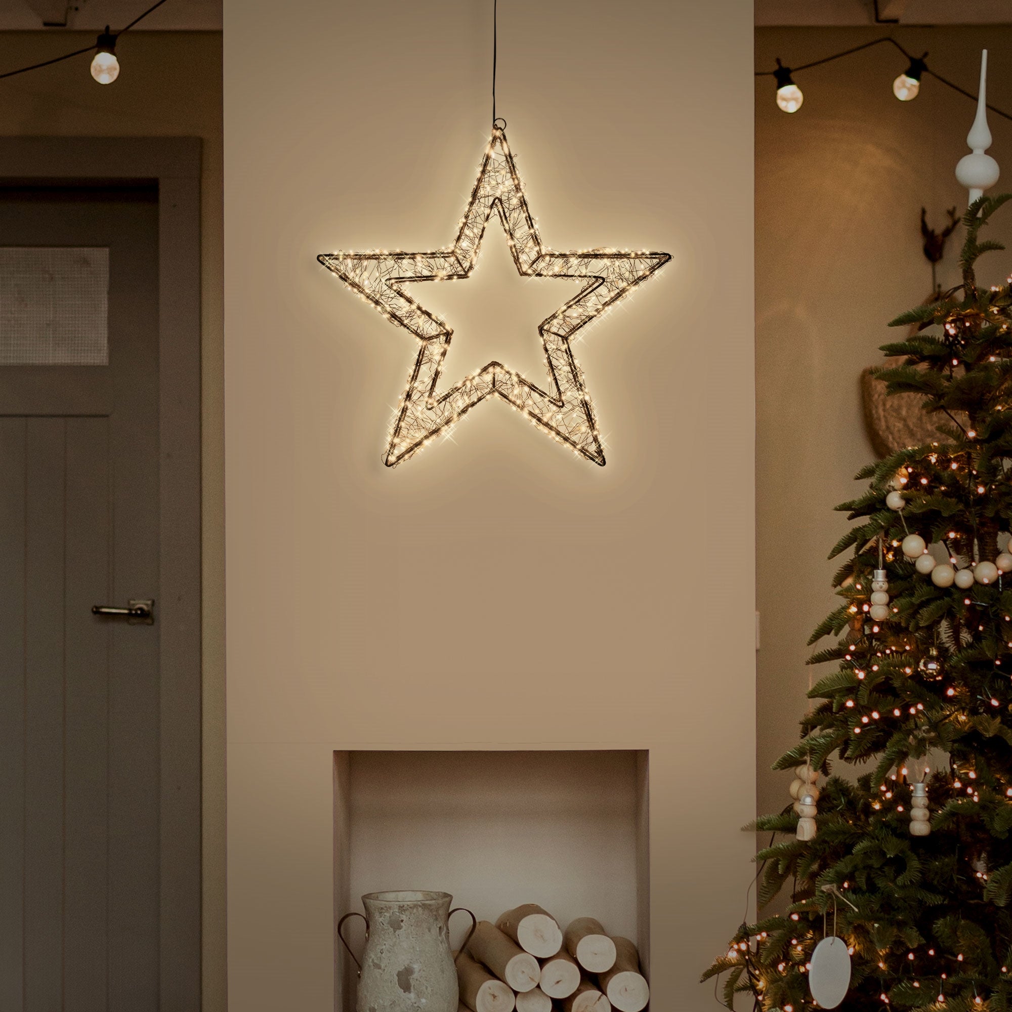 Une étoile illuminée est accrochée à un mur au-dessus d'un sapin de Noël.