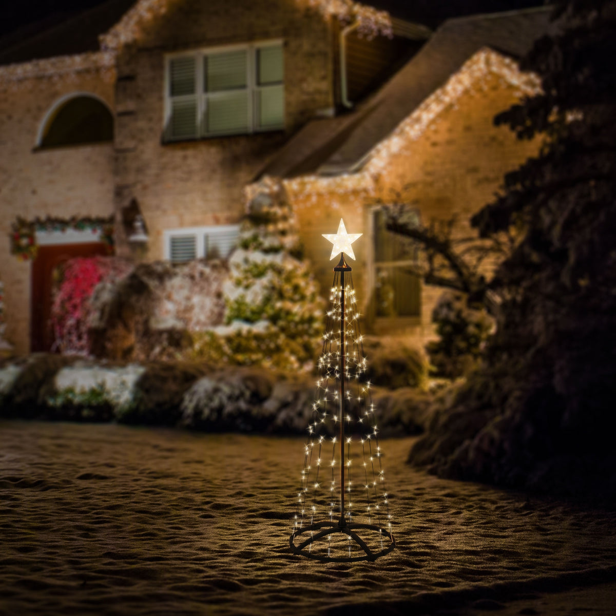 Ein beleuchteter Weihnachtsbaum mit Stern vor einem festlich geschmückten Haus.