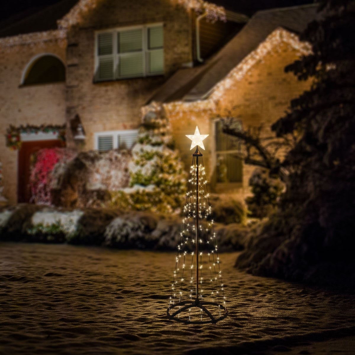 Ein beleuchteter Weihnachtsbaum mit Stern vor einem festlich geschmückten Haus.