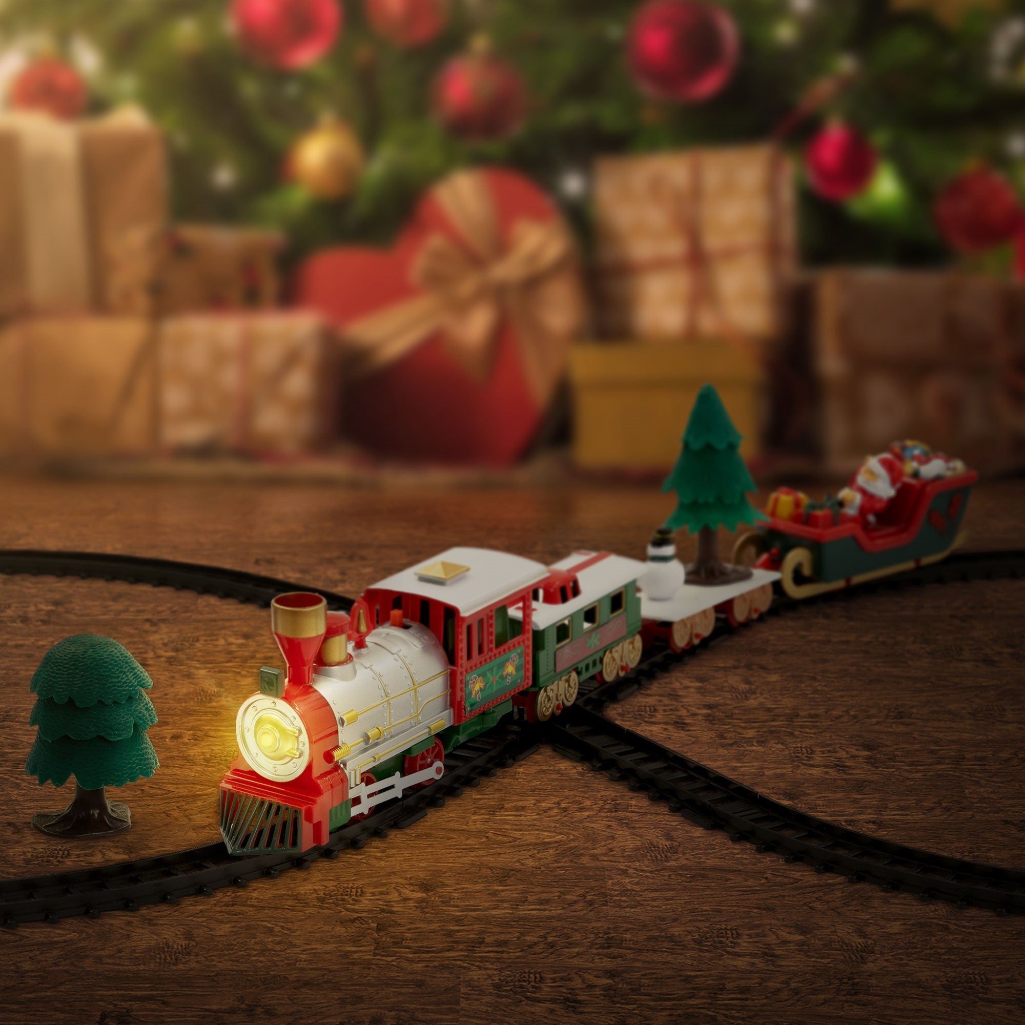 Spielzeugzug mit Lichtern und Tannenbäumen, vor einem Weihnachtsbaum und Geschenken.