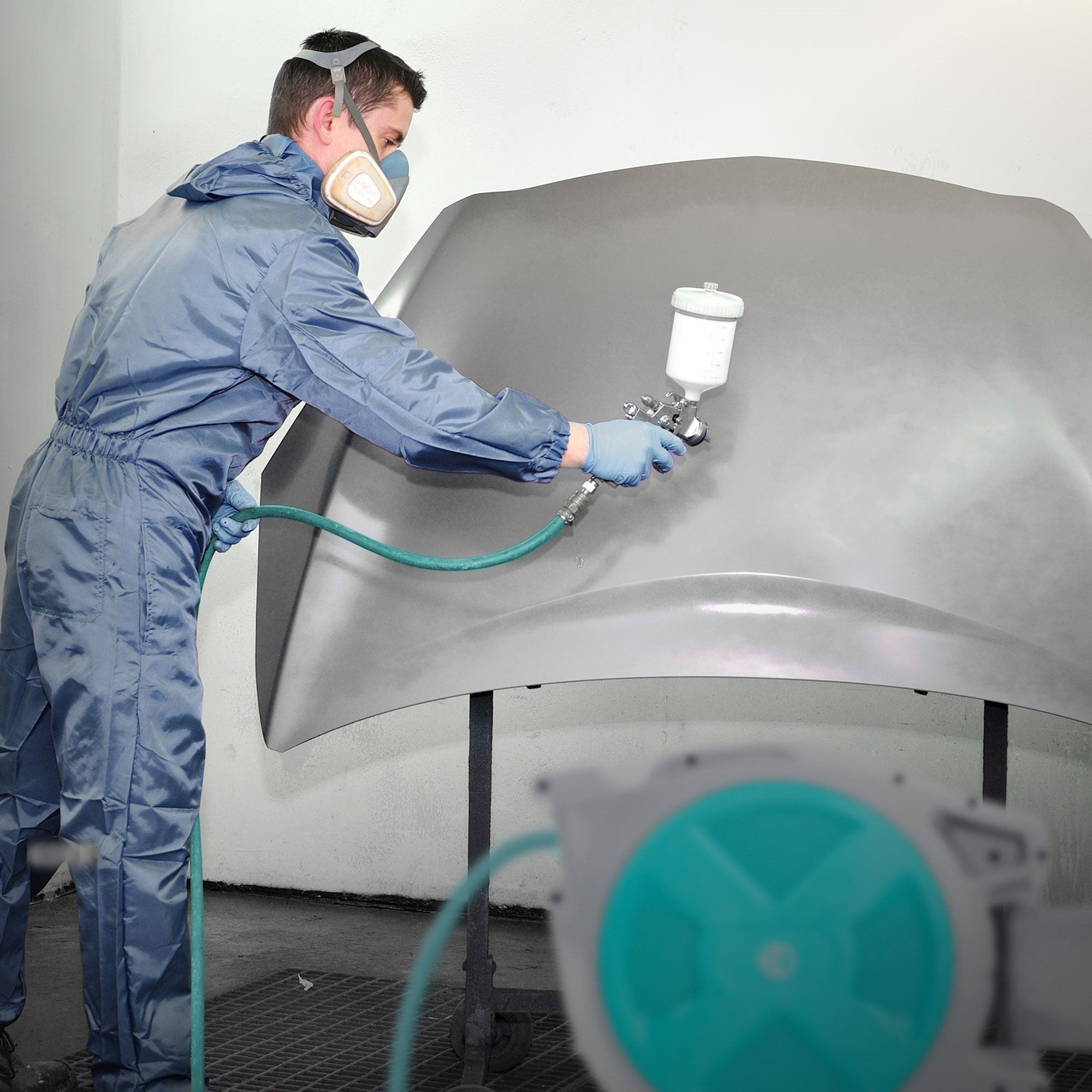 Mann in Schutzkleidung sprüht Farbe auf eine große graue Oberfläche.