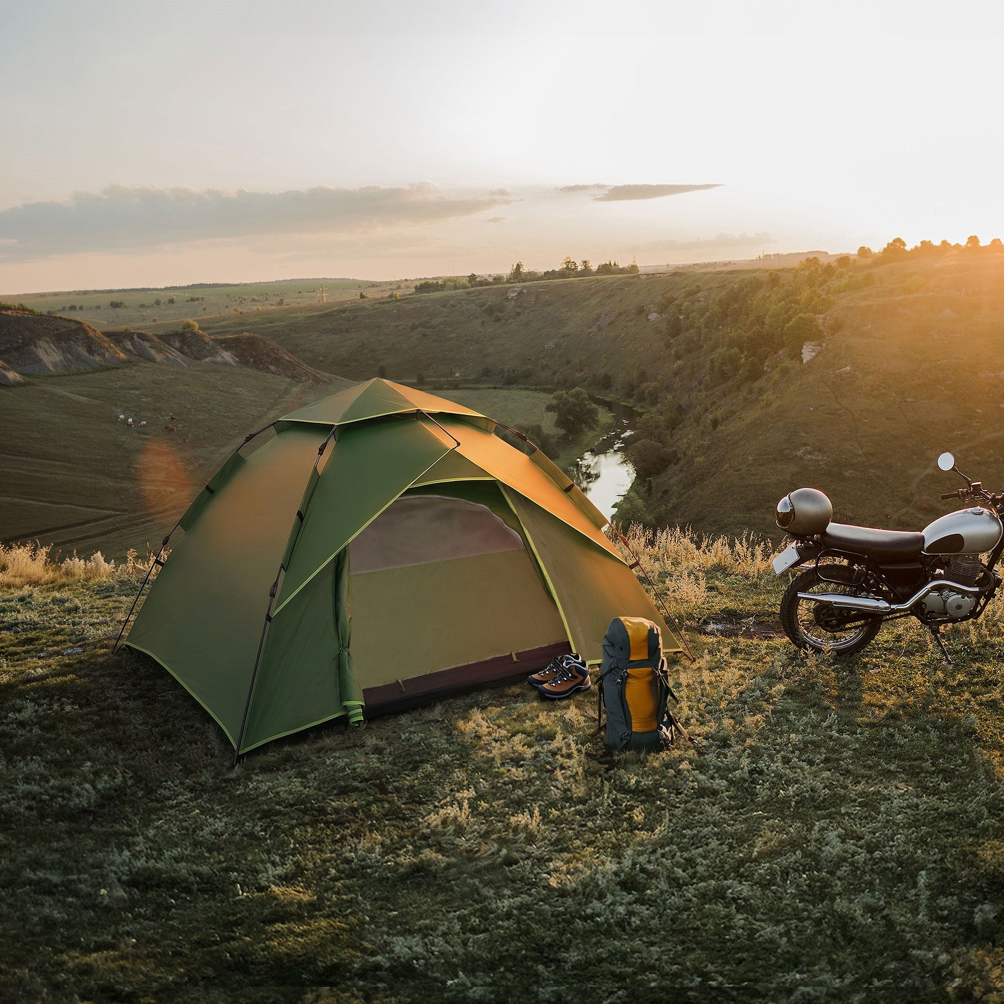Zelt in der Natur bei Sonnenuntergang, mit Rucksack und Motorrad in der Nähe.