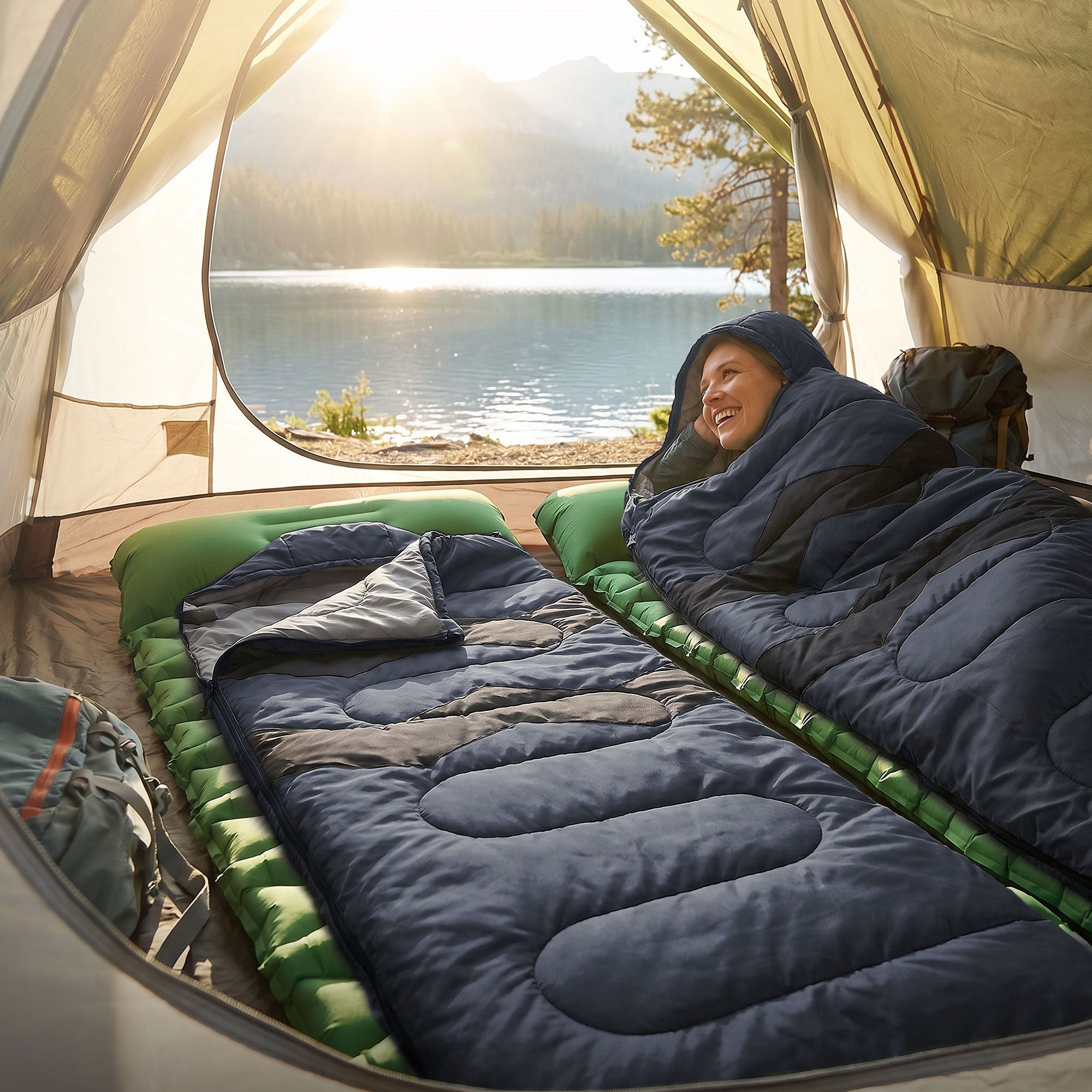 Eine Person in einem Schlafsack auf einer Schlafmatte, Blick auf einen See und Berge.